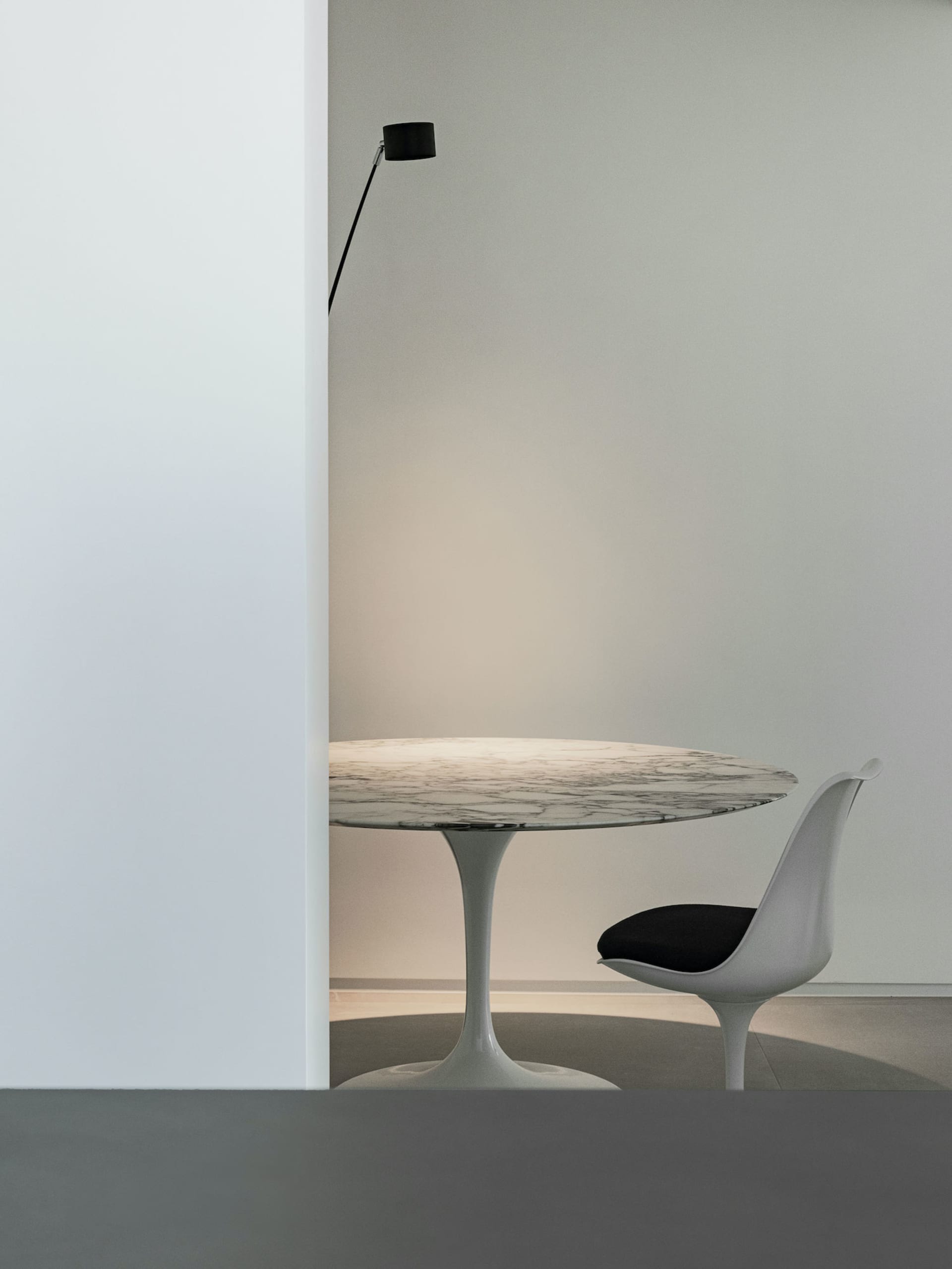 A minimalist modern dining room featuring a round marble table with a sleek, white tulip base and a single white chair with a