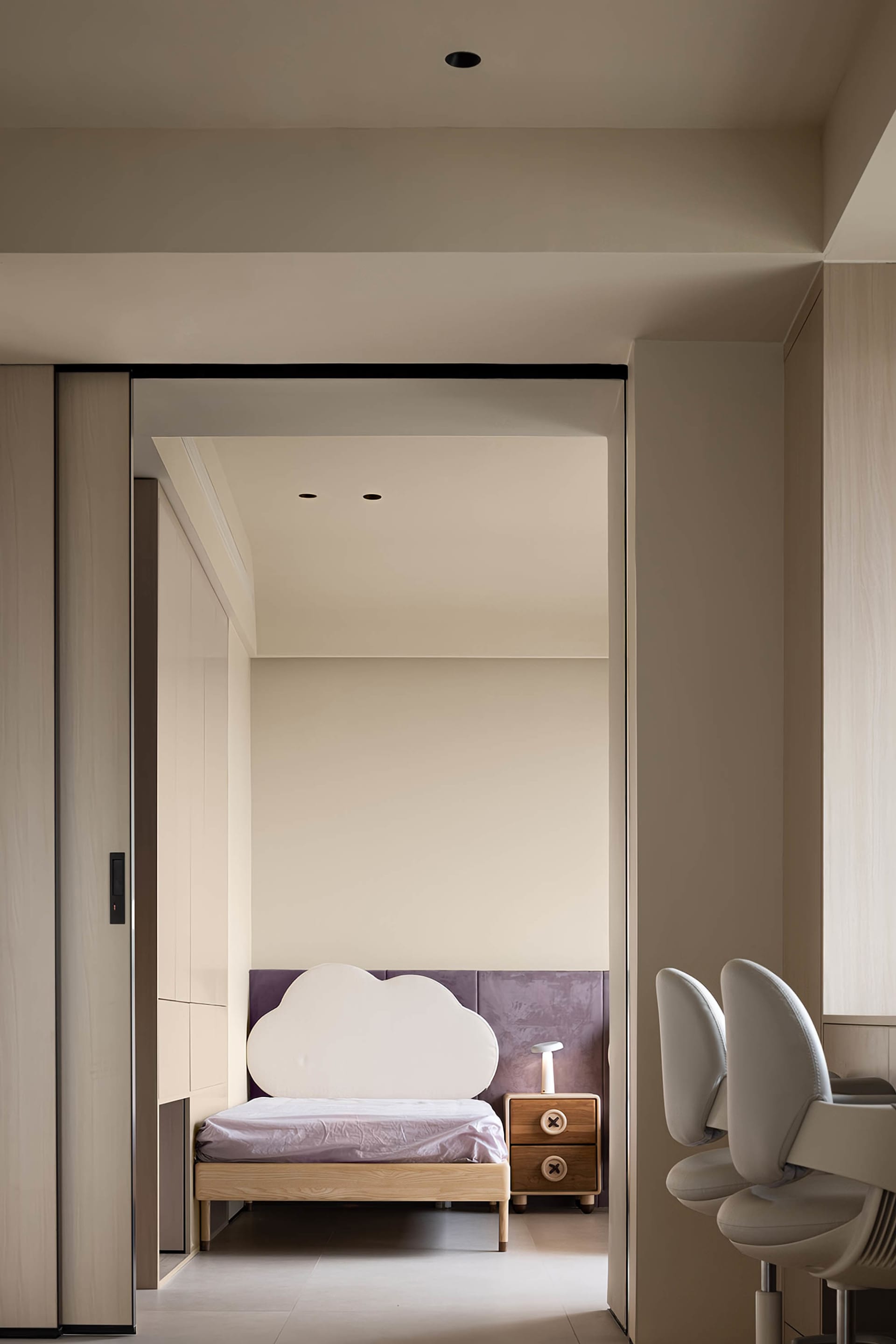 A minimalist bedroom featuring a cloud-shaped headboard, purple upholstered wall, and wooden nightstand.
