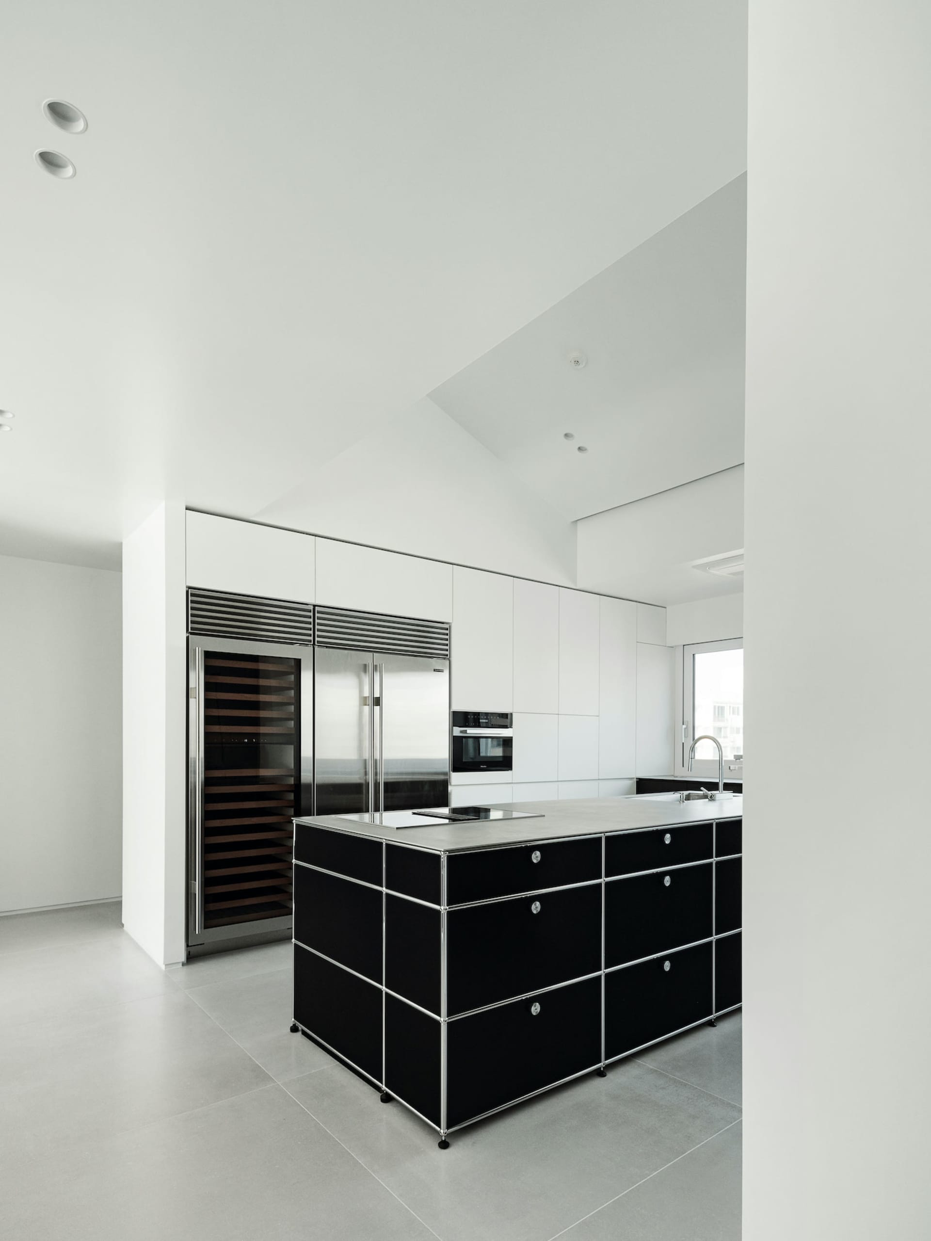 A modern minimalist kitchen featuring stone countertops and a black island with a sink and stove.