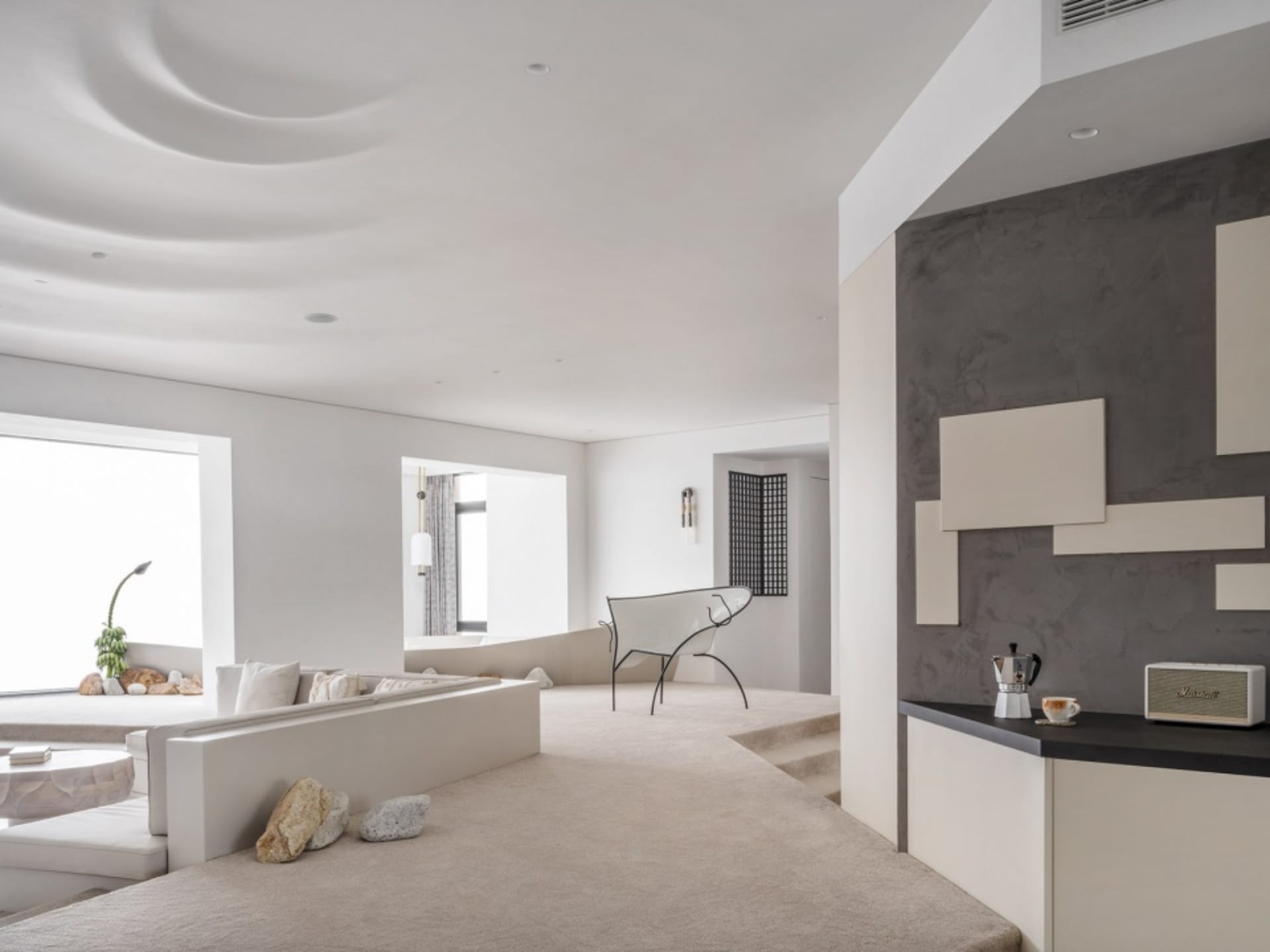 A modern minimalist living room with concrete flooring and walls, featuring a white couch, a white chair, and a concrete wall