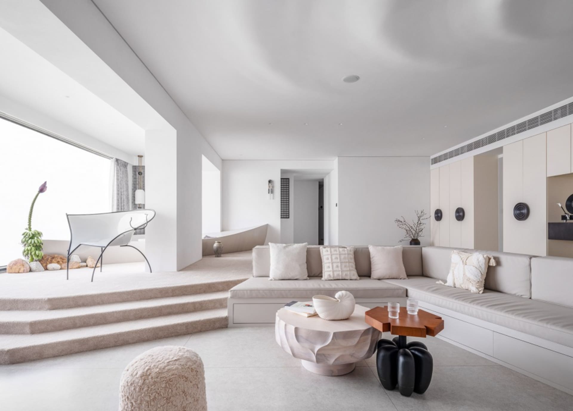 A minimalist living room with neutral-toned tiles, a white sectional sofa, and a combination of white and wooden furniture.