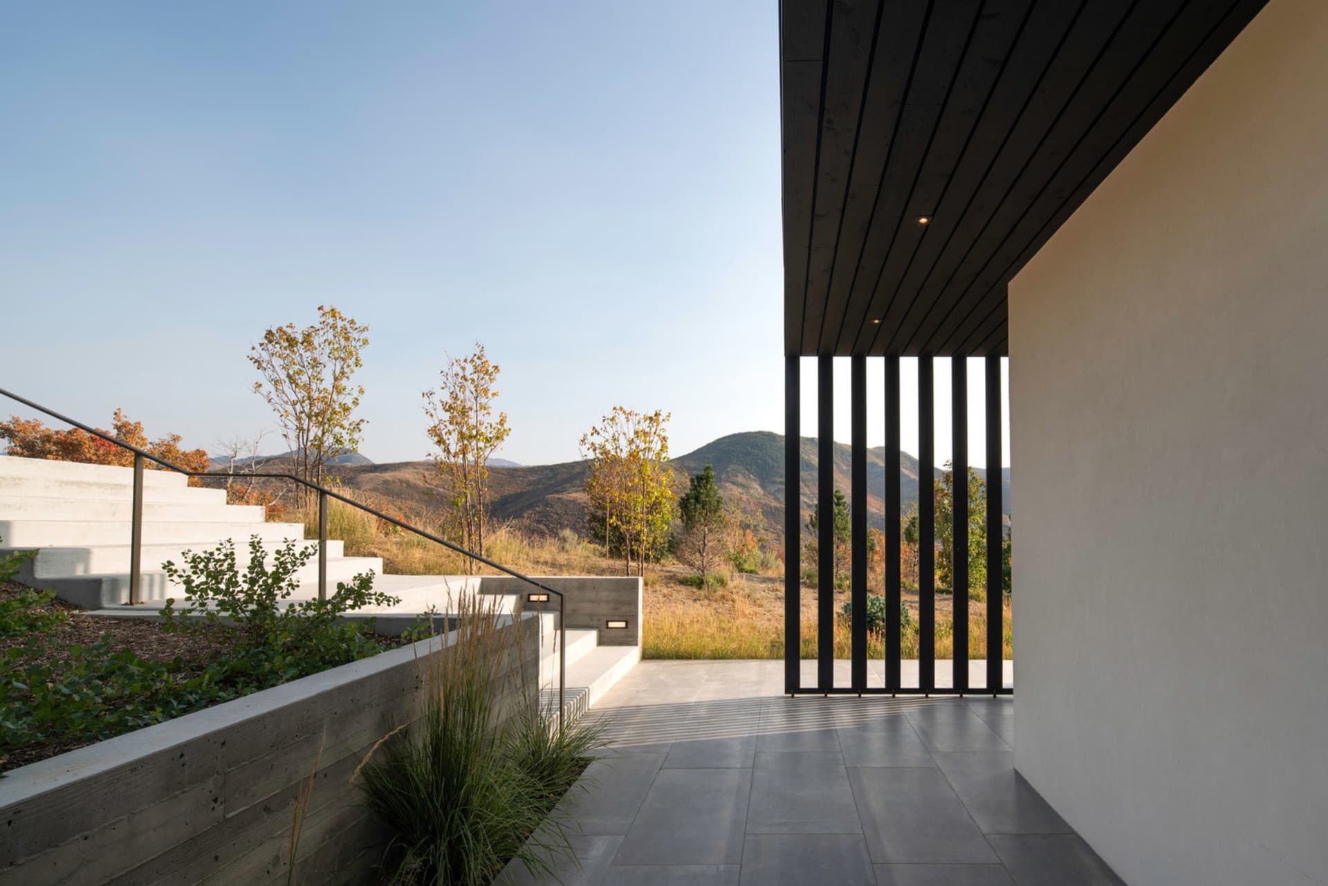 Concrete stairway with a modern design featuring a black metal railing and a view of the surrounding landscape and mountains.