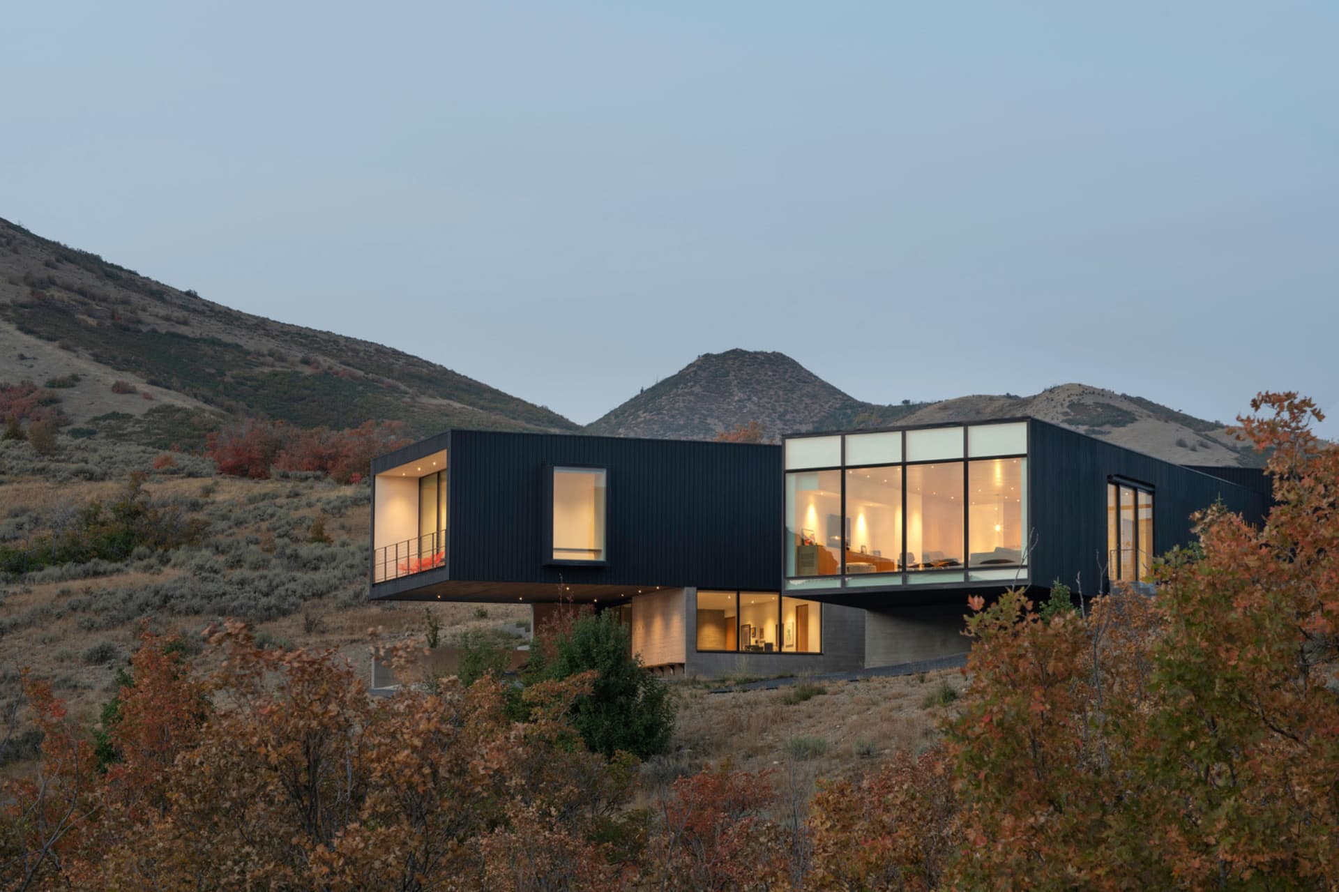 Modern residential building with a metallic facade and large glass walls set against a mountainous landscape.