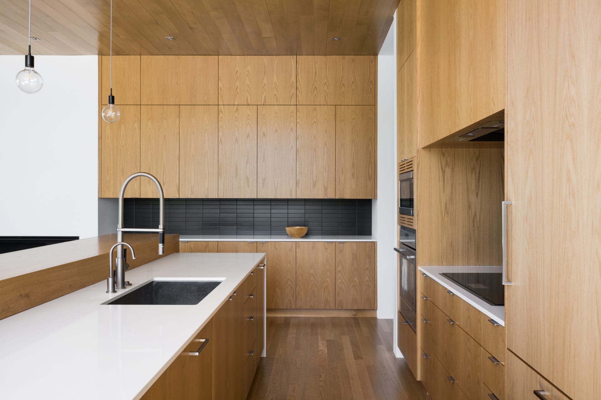 A sleek, modern residential kitchen featuring wooden cabinetry and white countertops.