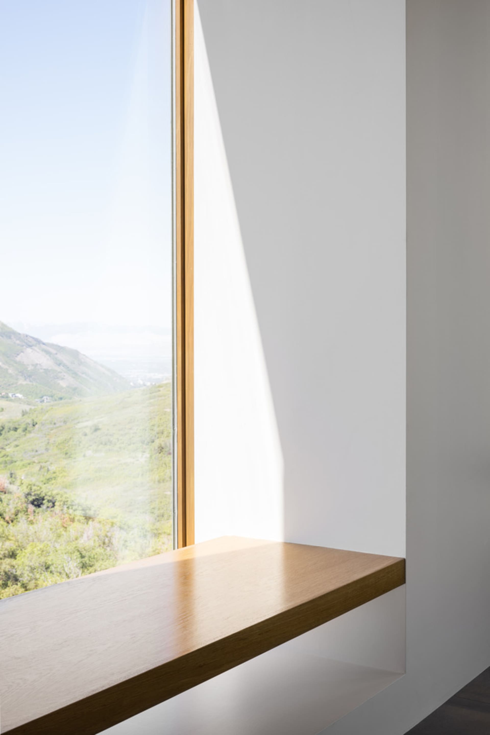 Modern interior design featuring a window seat with a white wall and a glass window overlooking a mountain view.