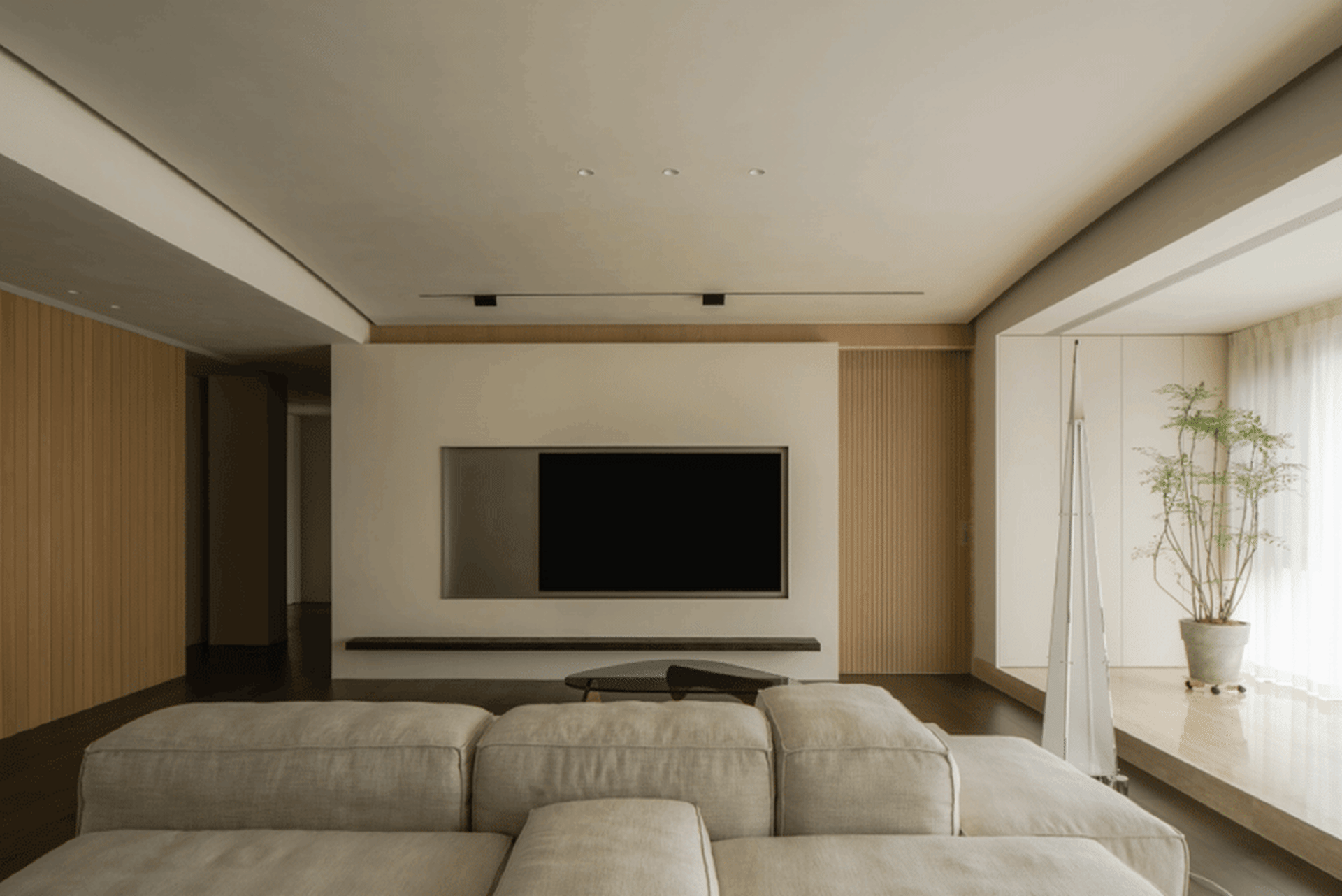 Modern minimalist living room with a neutral color palette, a sleek grey sofa, and a mounted television on the wall.