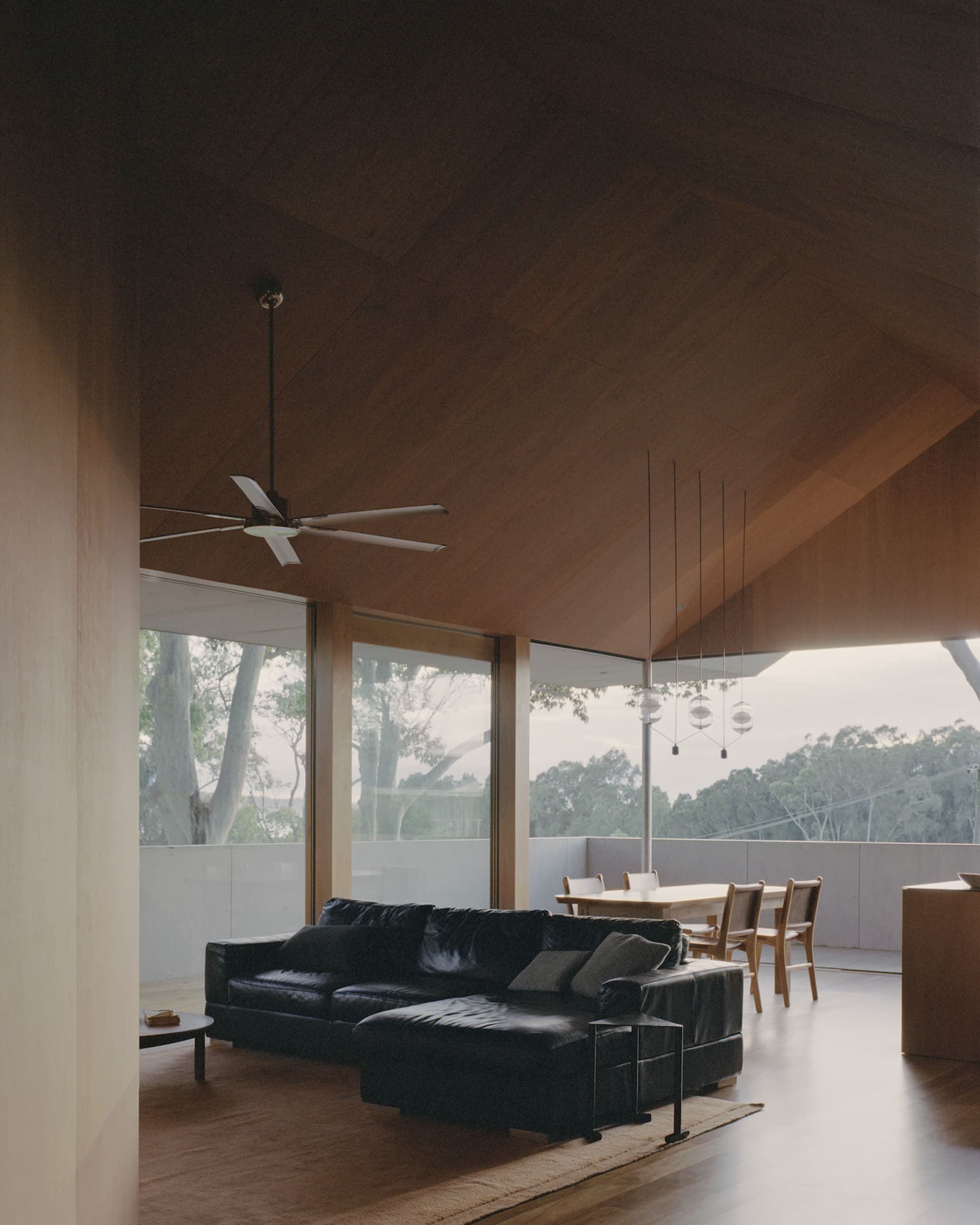 A modern living room featuring wooden walls, a black leather sectional sofa, and a glass table with chairs.
