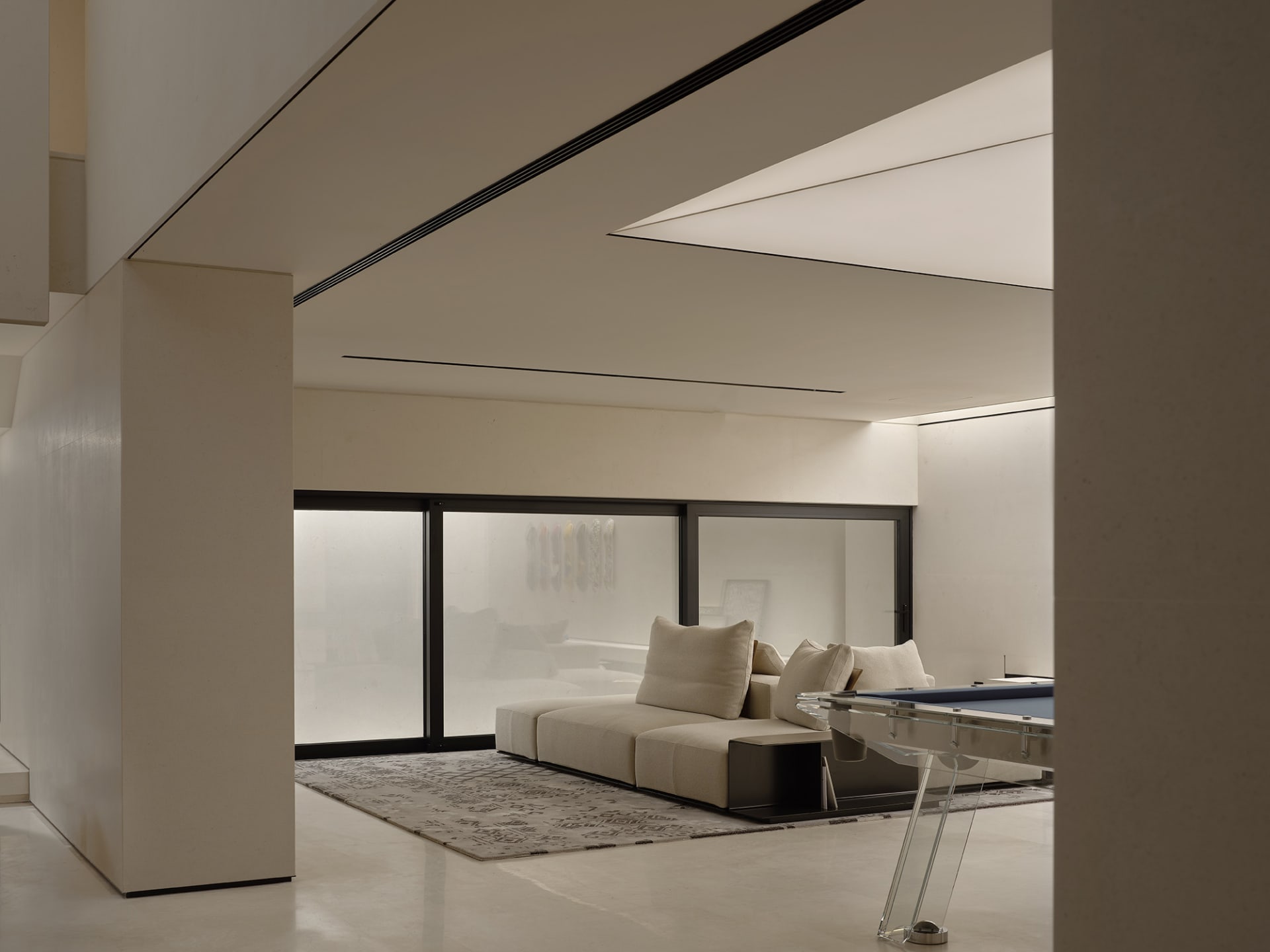 Modern minimalist living room with concrete and glass materials, featuring a contemporary sofa and floor-to-ceiling windows.