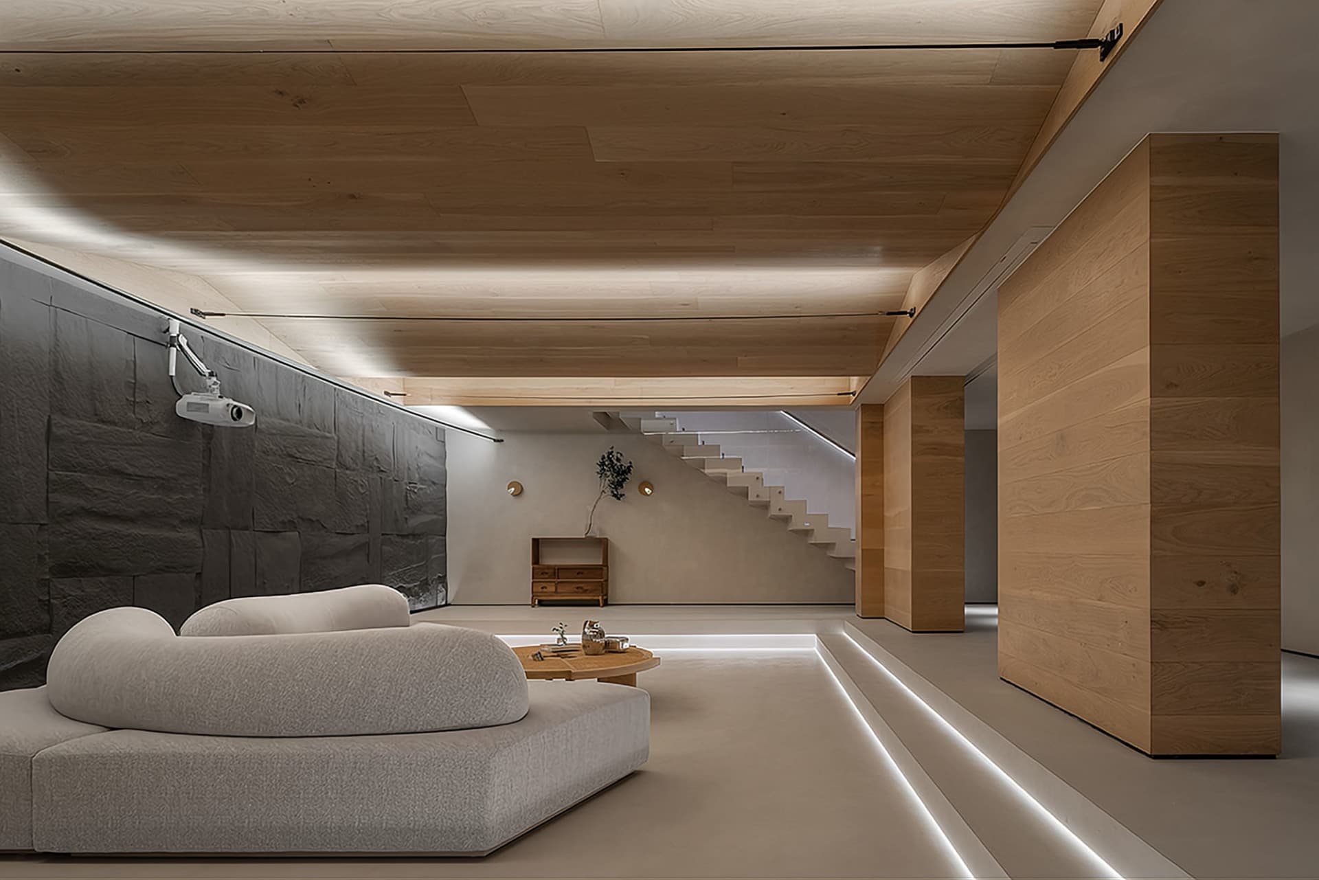 A modern minimalist living room with a white sofa, a round wooden coffee table, and a projector setup on a black, stone-like