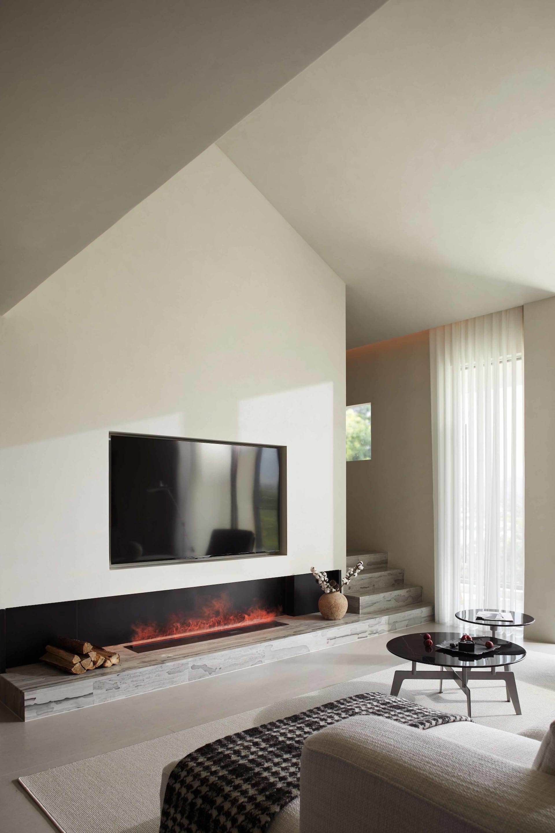 A minimalist modern living room with a white interior and fireplace, featuring elegant furniture and a simple, well-lit desig