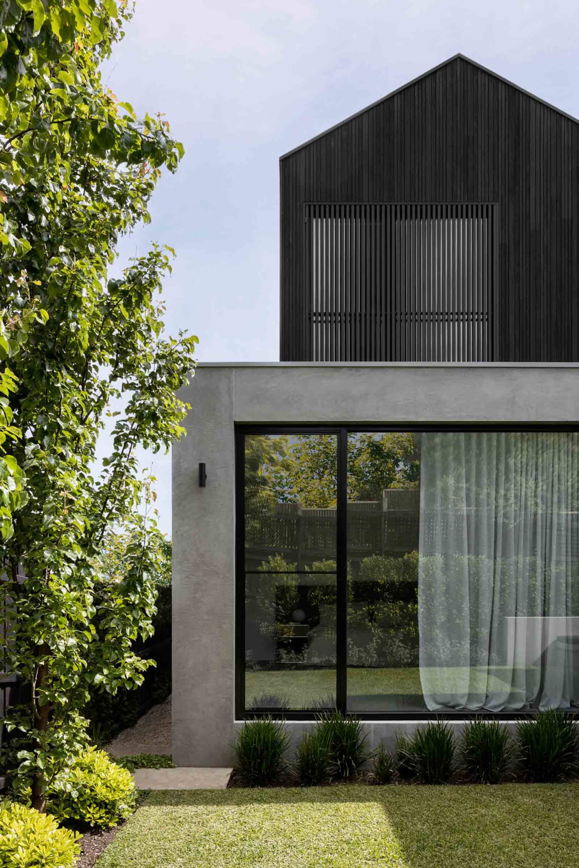 Modern house with concrete and glass exterior, featuring a black roof and large windows.