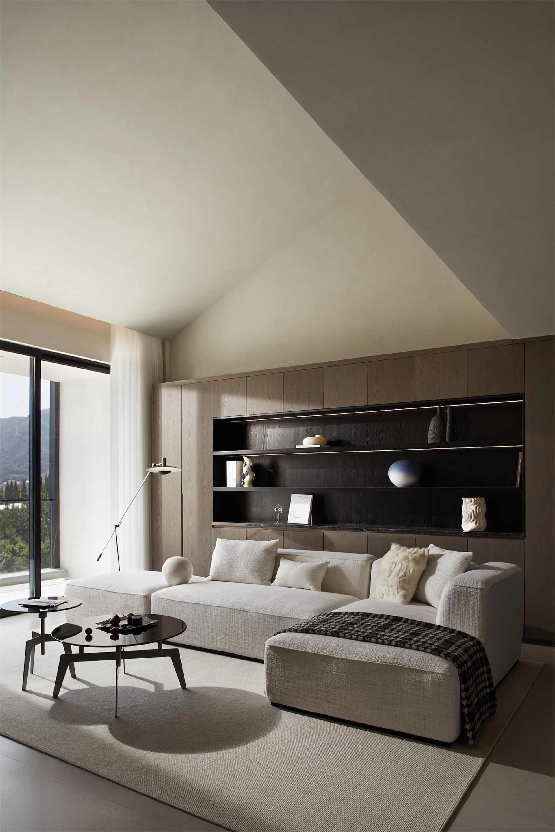Modern minimalist living room featuring a white sectional sofa, black coffee table, and dark wooden shelves.