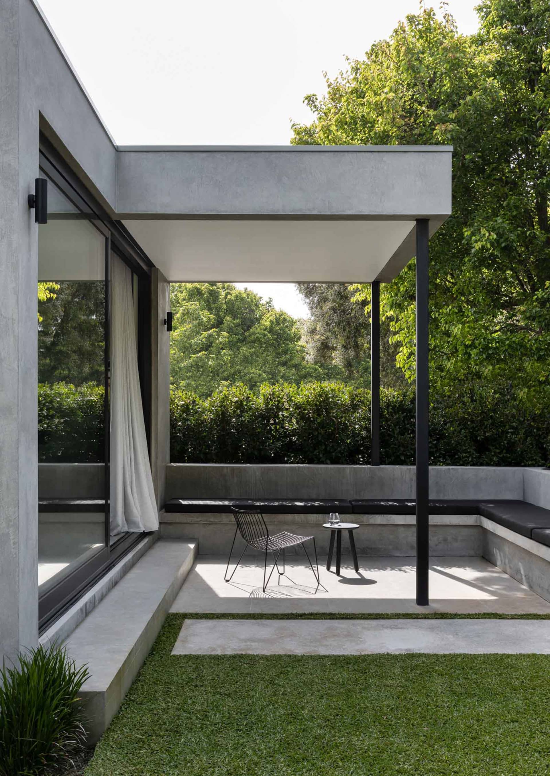 Modern minimalist patio area with concrete seating and black metal frame furniture