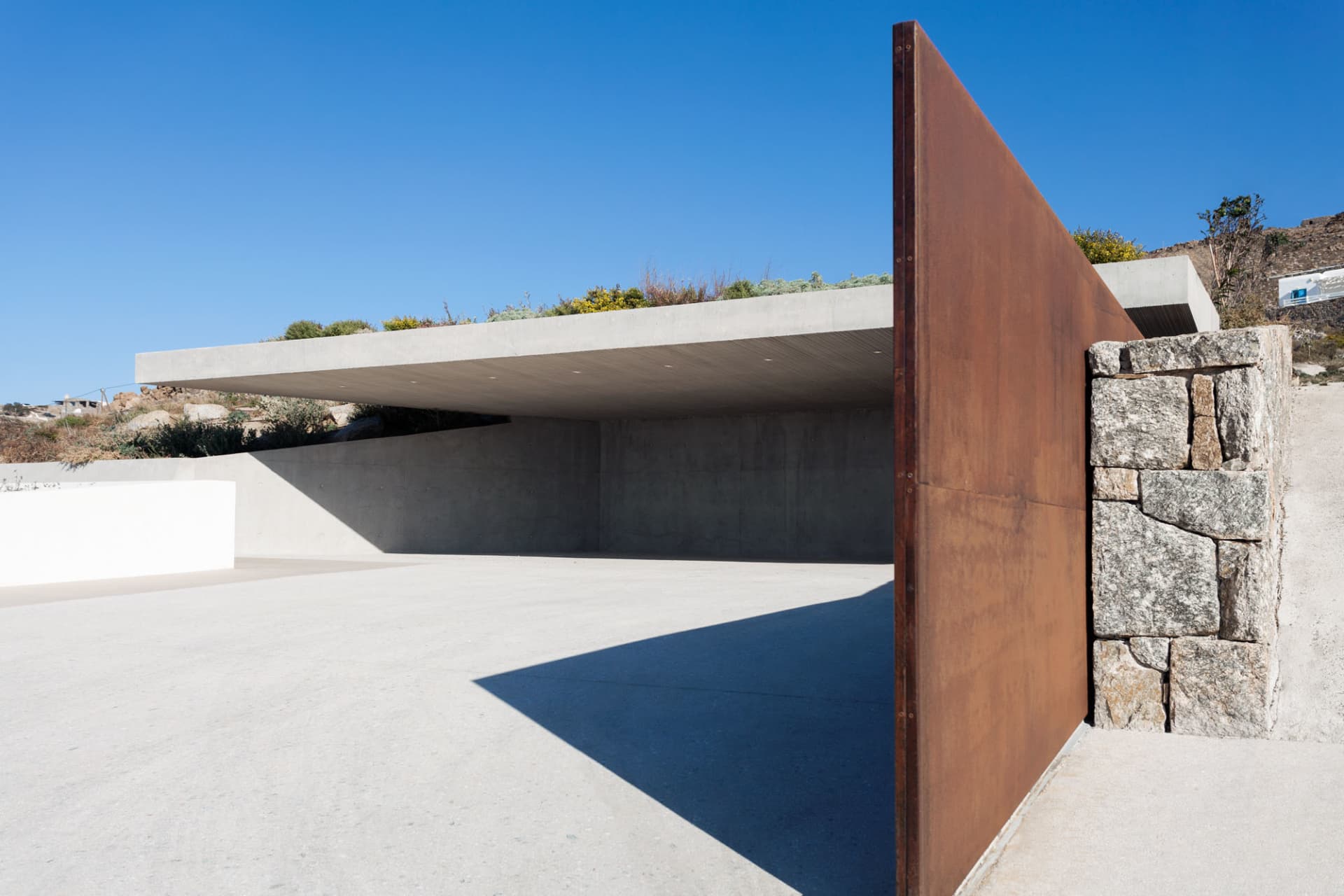 A modern concrete architectural exterior featuring a red-detailed metal edge structure.