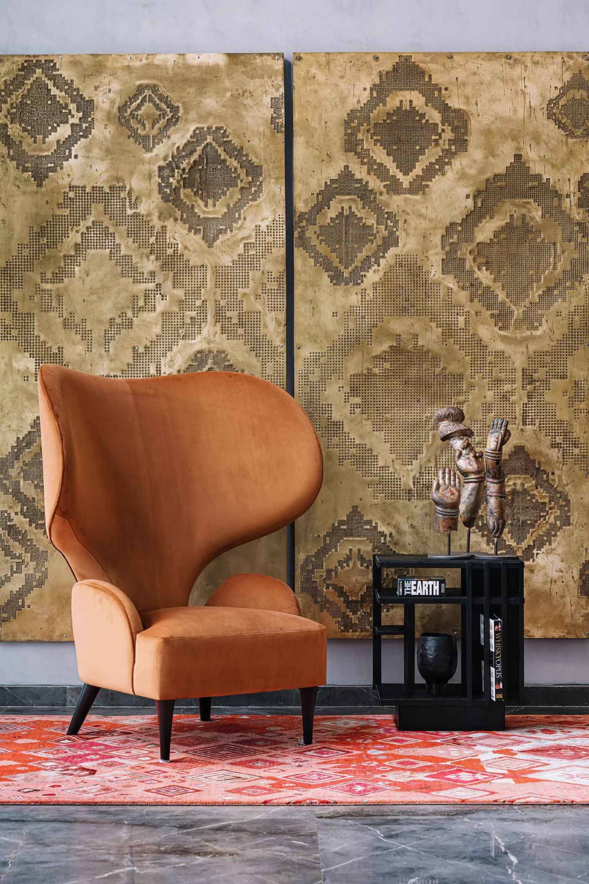 A modern living room featuring a velvet armchair and patterned wallpaper.