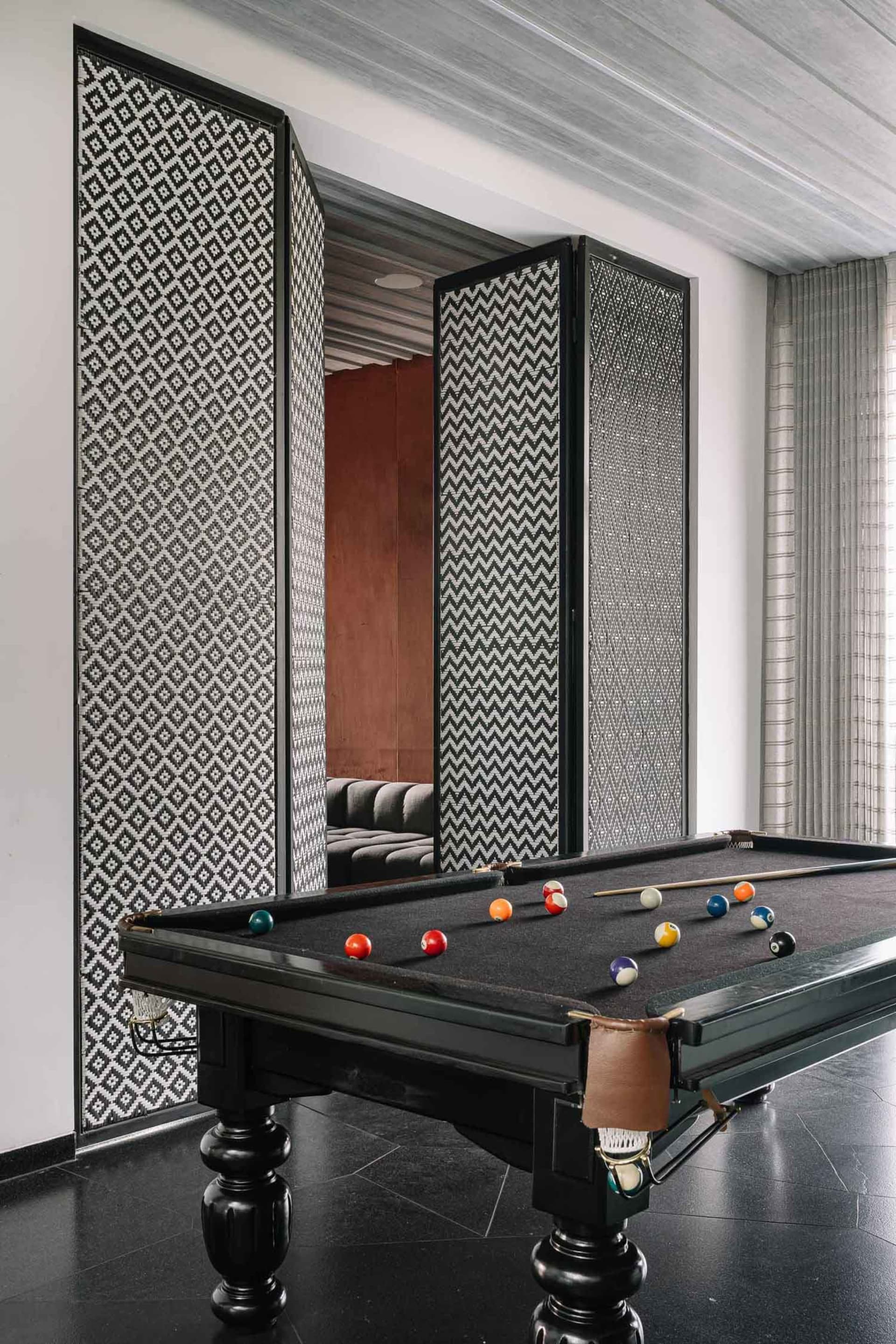 An industrial-style pool room with a black concrete floor, a pool table with billiard balls, and decorative floor-to-ceiling