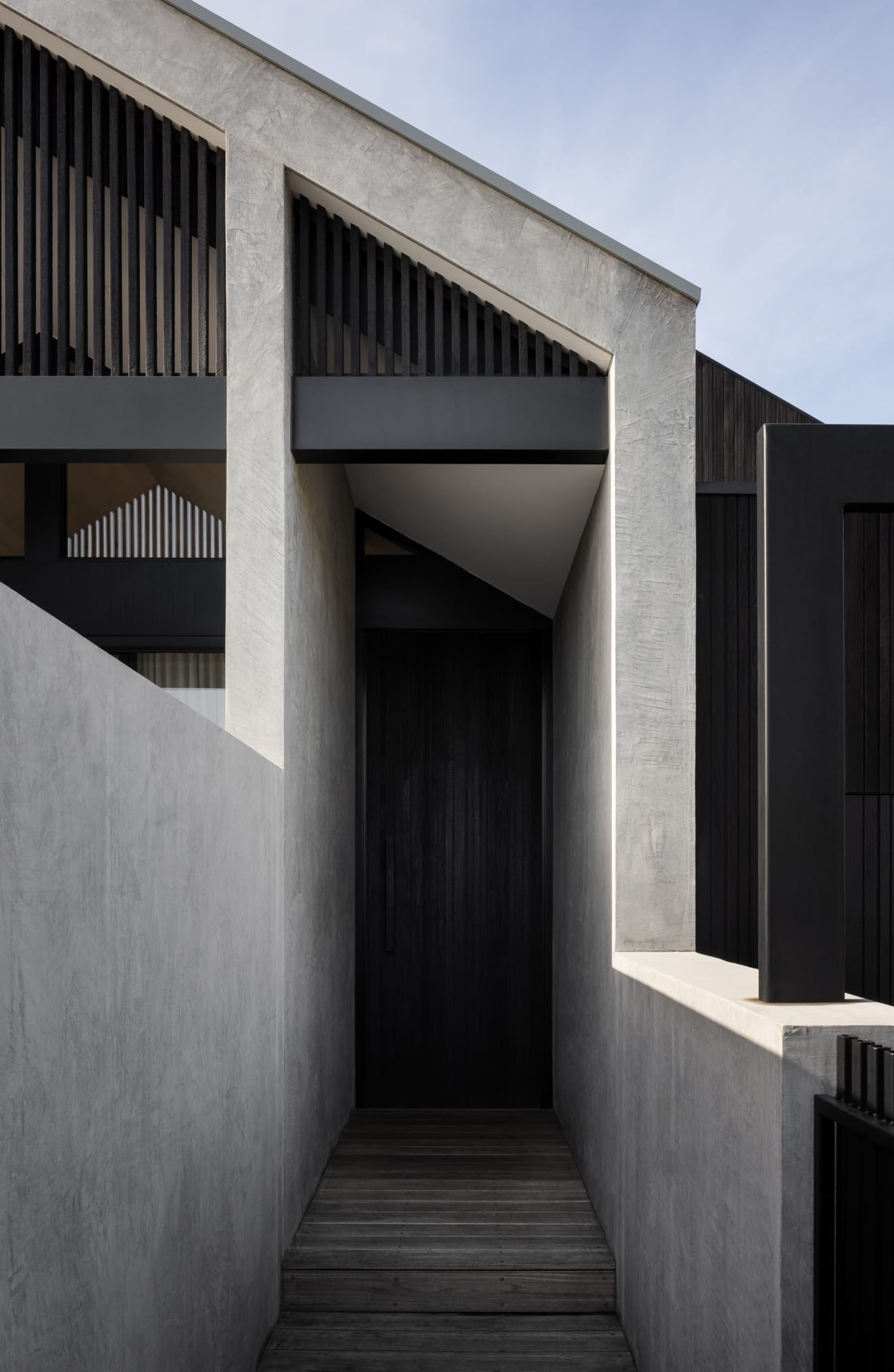 Contemporary concrete entryway with wooden flooring and black metal railings.