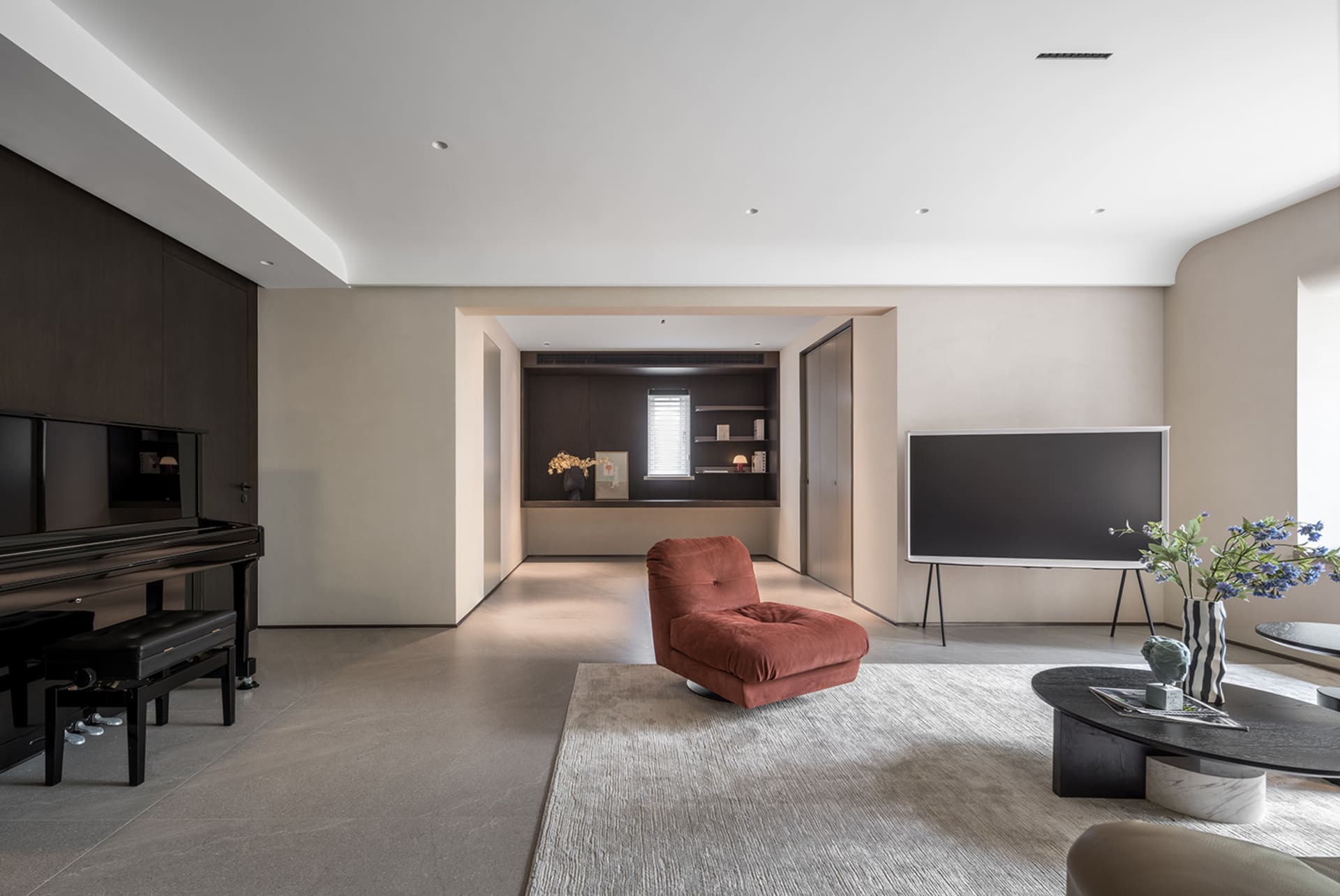 A modern living room with concrete flooring, minimalist decor, and a single red plush chair.