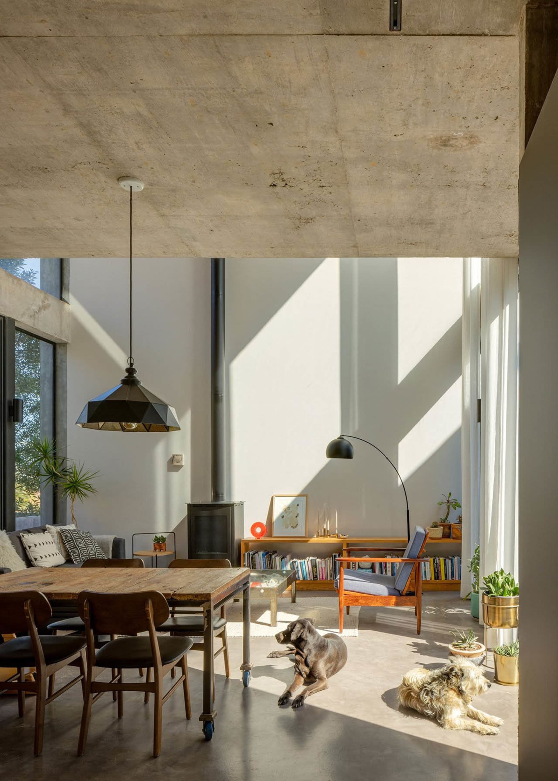 Living room with concrete floor, wooden table, industrial pendant light, and concrete beams.