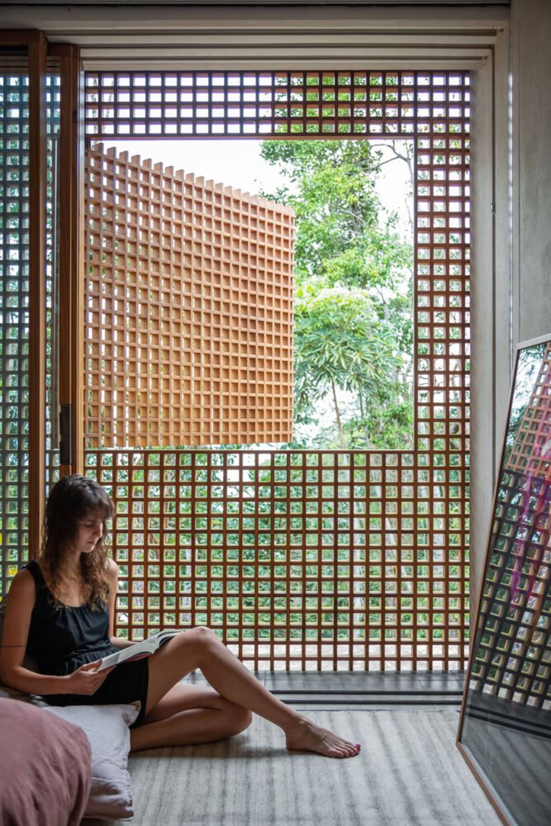 A woman sitting cross-legged on the floor in a modern residential living room with natural light and a wooden lattice frame.