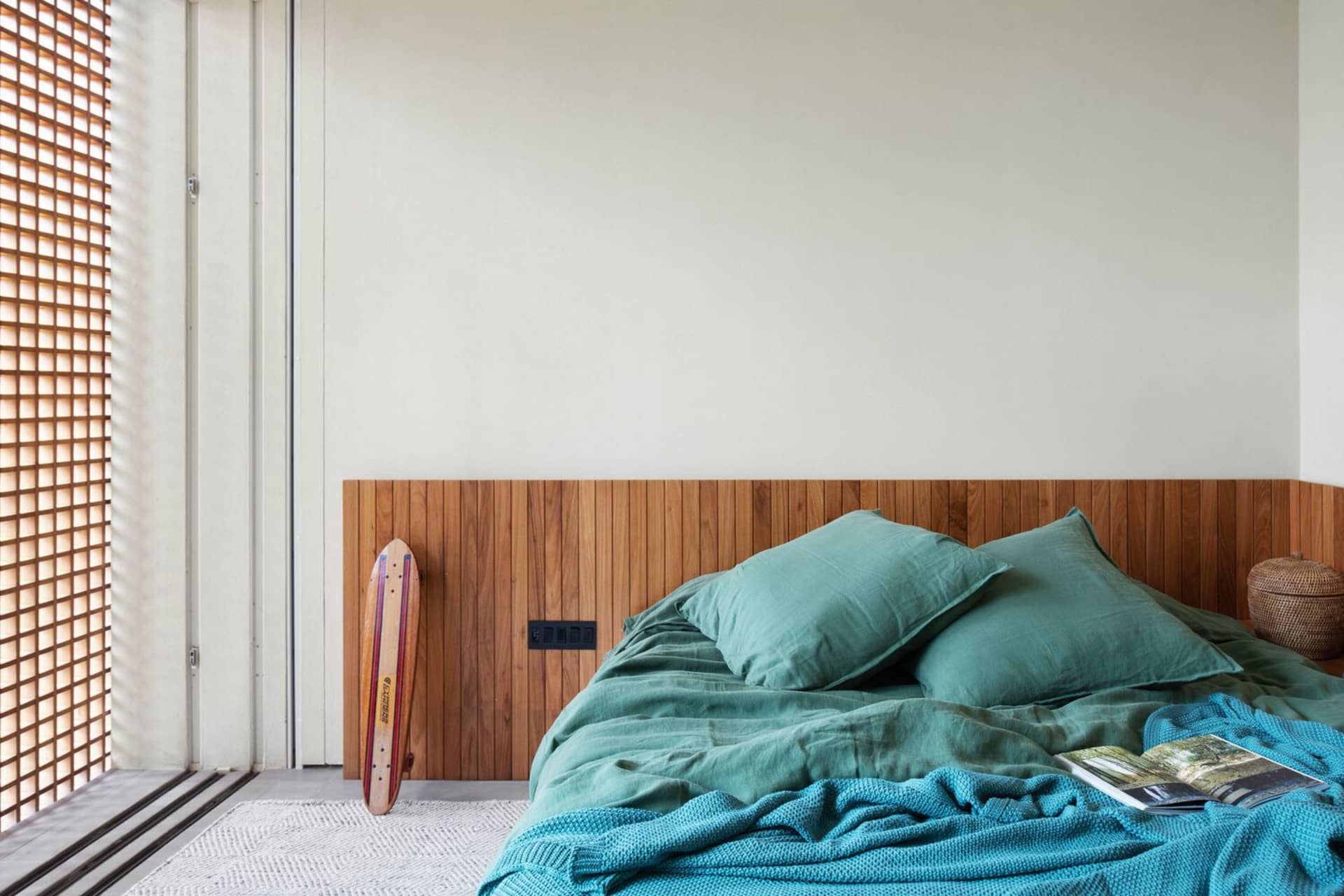 Minimalist bedroom featuring teal bed linens and a wooden headboard.