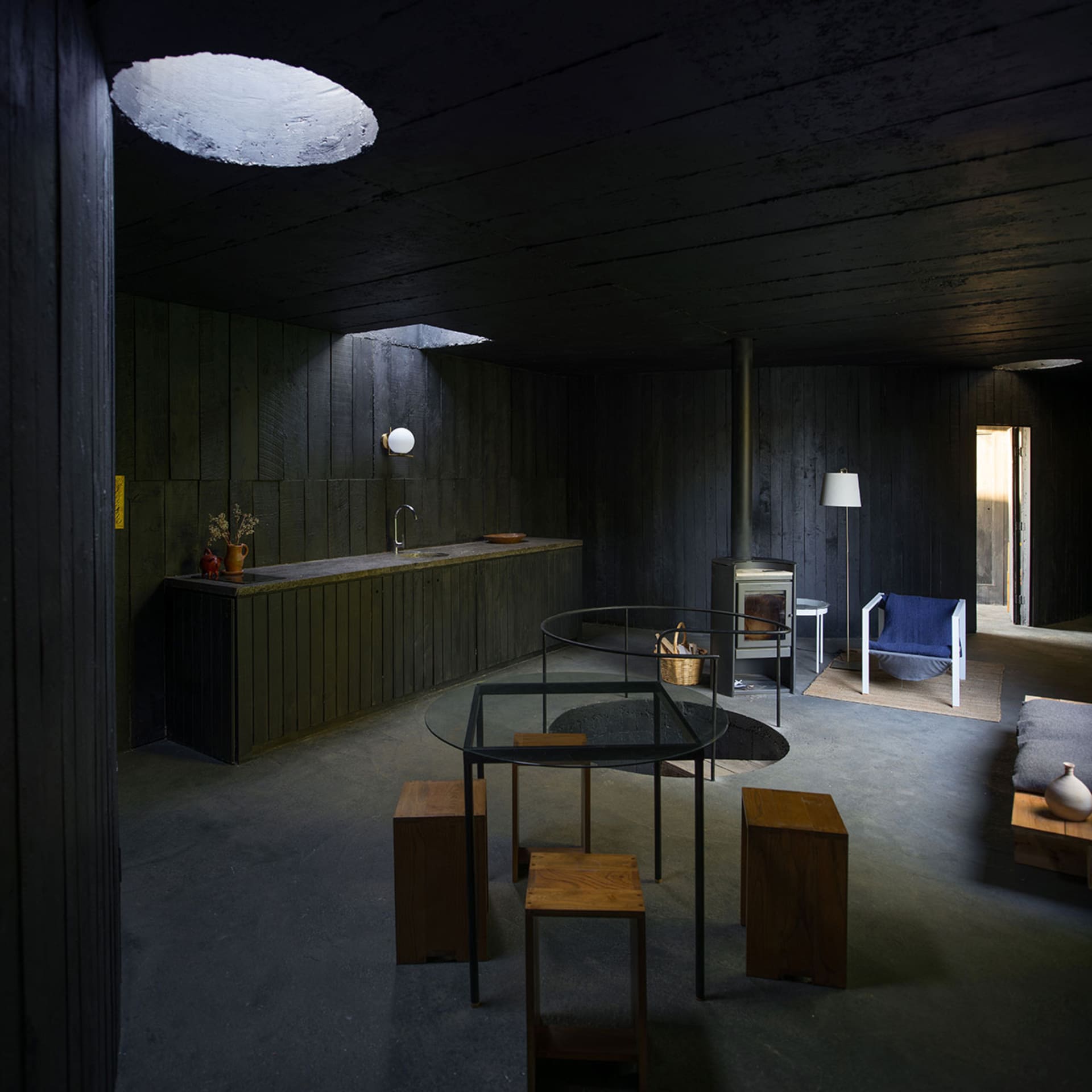 A minimalist kitchen with a concrete floor, walls, and table, and wooden stools.