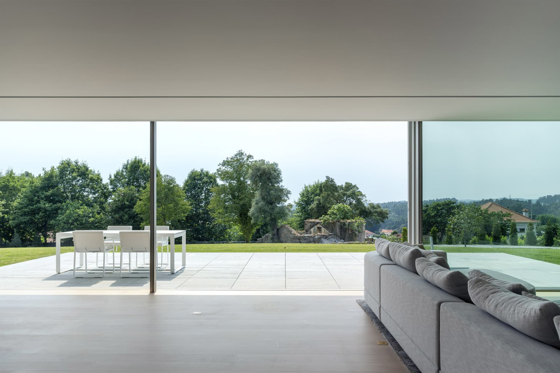 Modern minimalist living room with a large glass wall overlooking a lush green landscape.