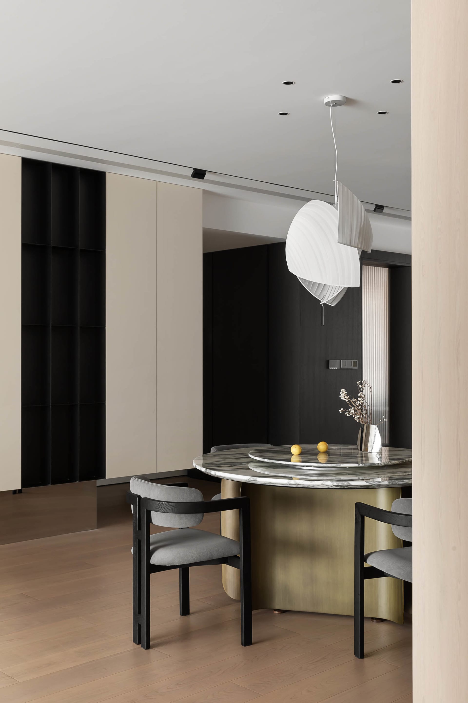 Modern dining space featuring white marble table with brass legs, black chairs, and minimalist pendant light.