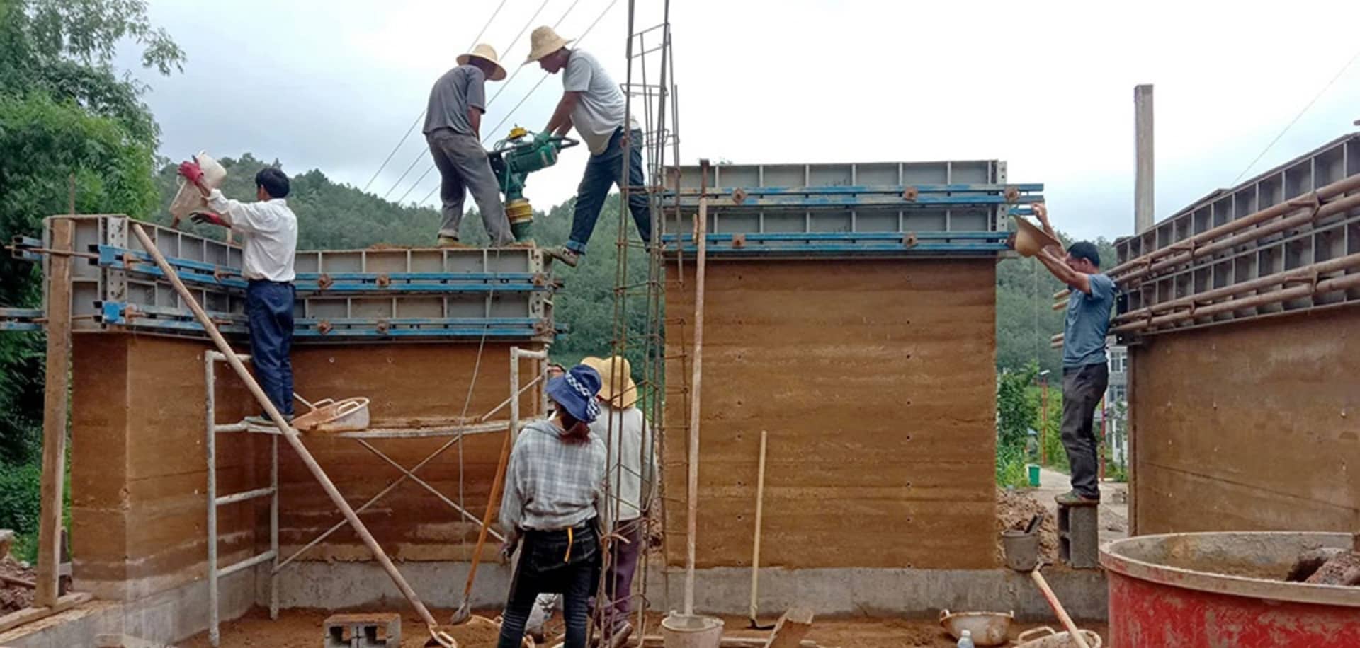 Workers on a construction site using concrete blocks and scaffolding for building a wall.