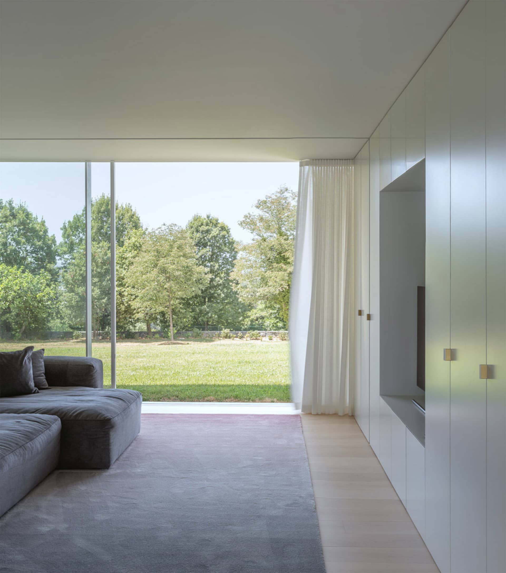 Modern minimalist living room featuring a glass wall, concrete floor, and fabric furniture.