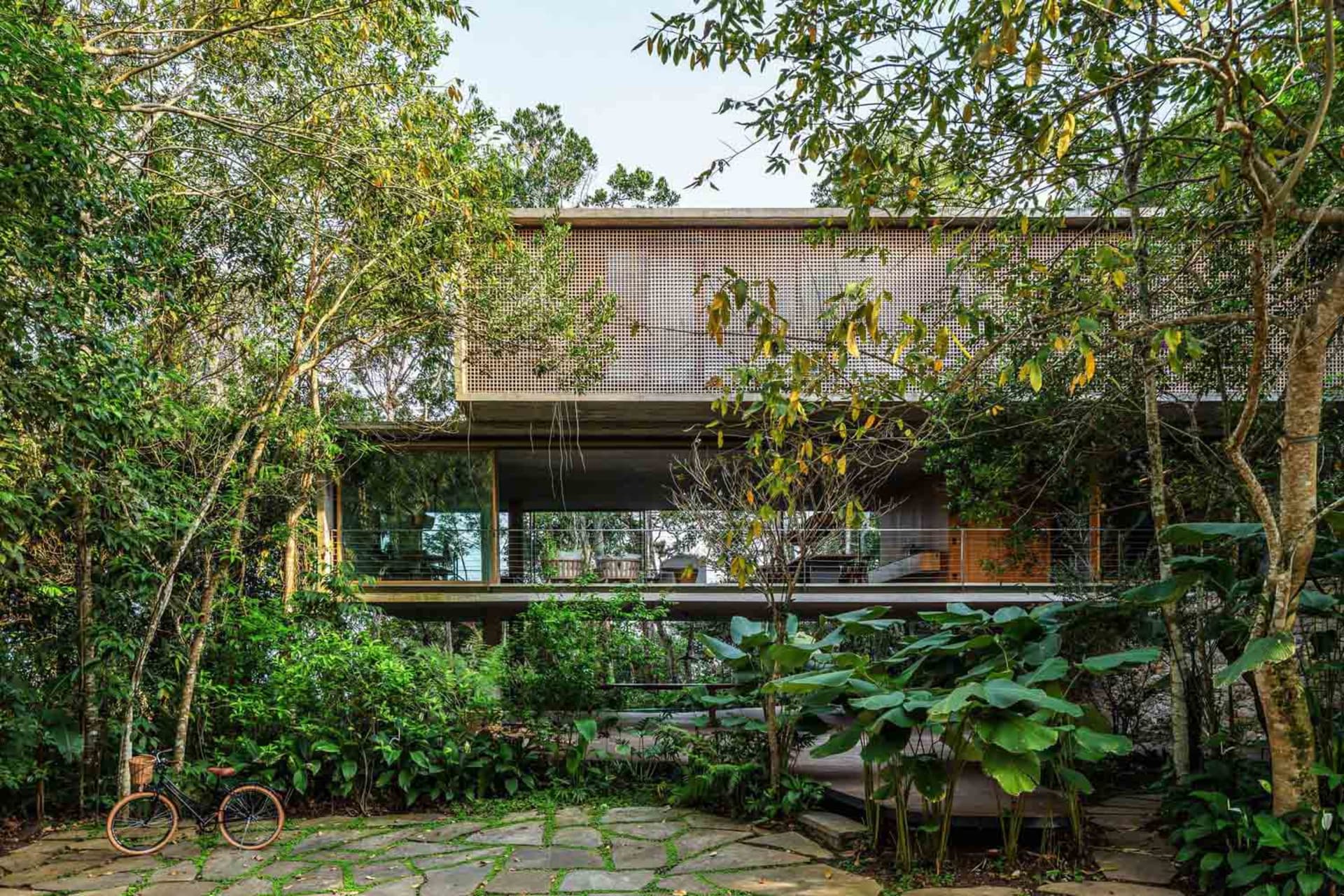 Modern house exterior featuring wooden panels and large windows, surrounded by lush greenery.