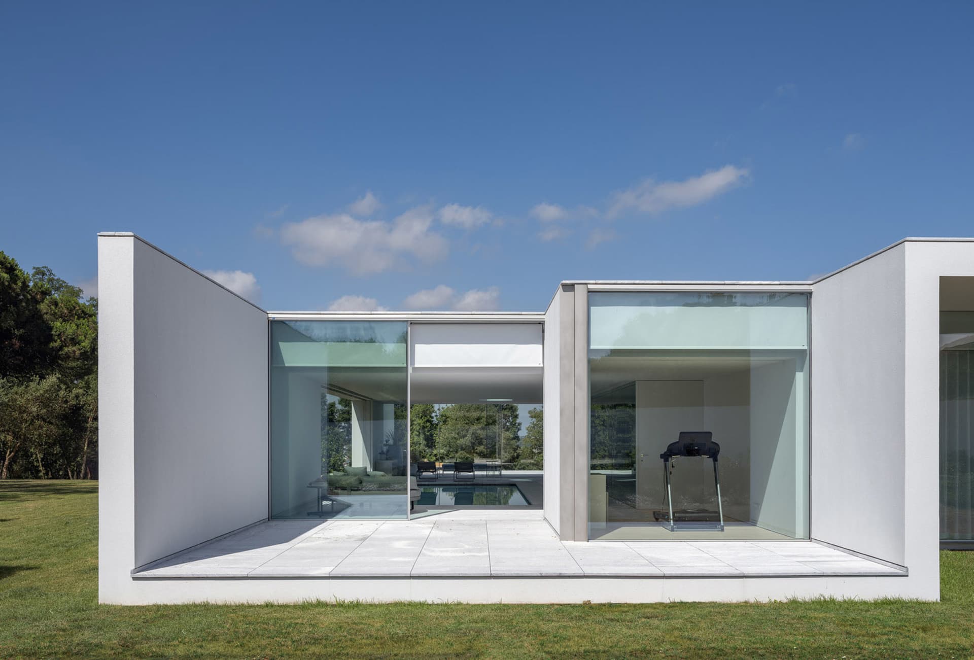 Modern residential exterior with glass walls and concrete patio, featuring a minimalist design.