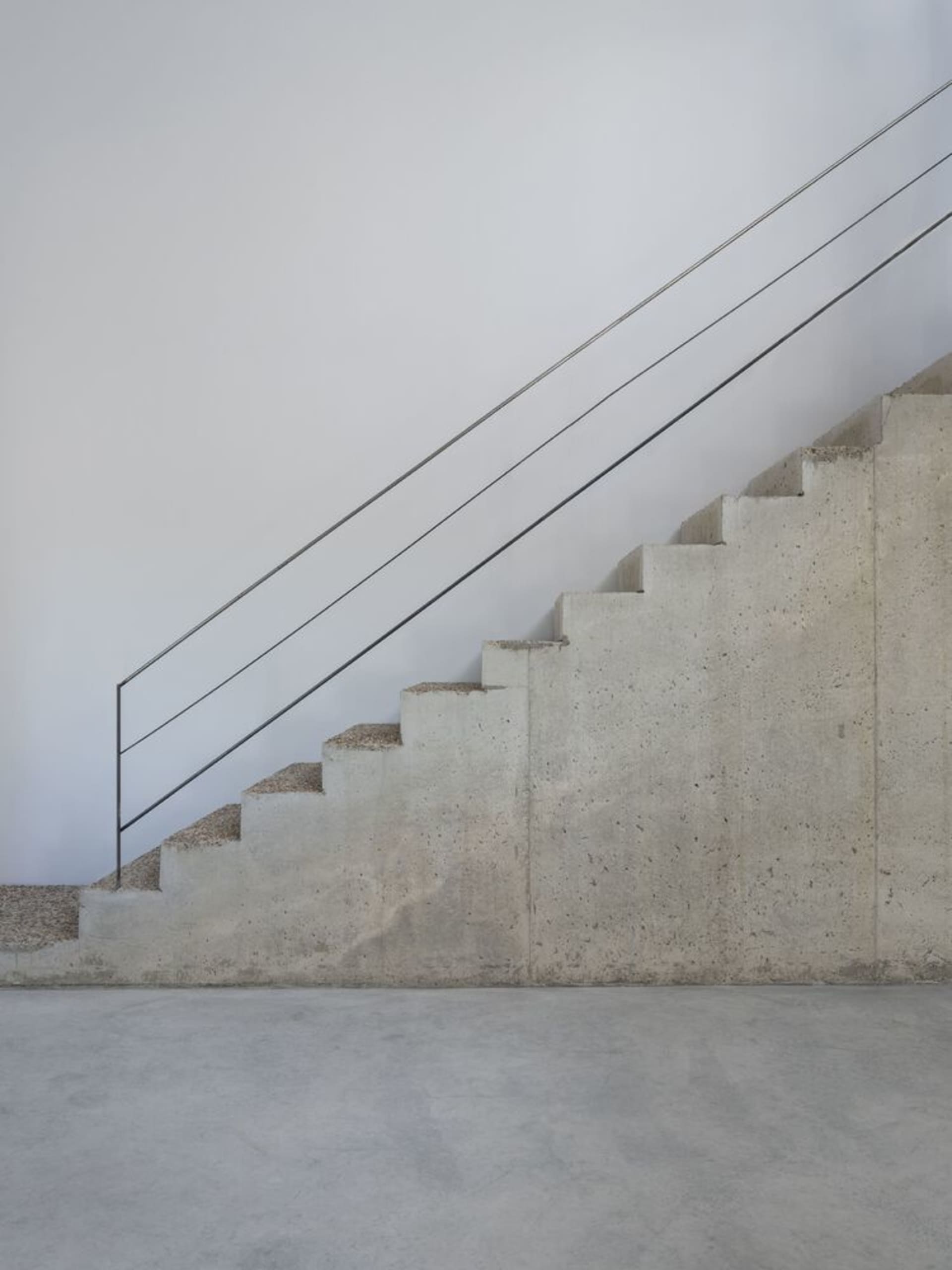 Minimalist, industrial-style staircase with concrete steps and a steel handrail against a white wall.