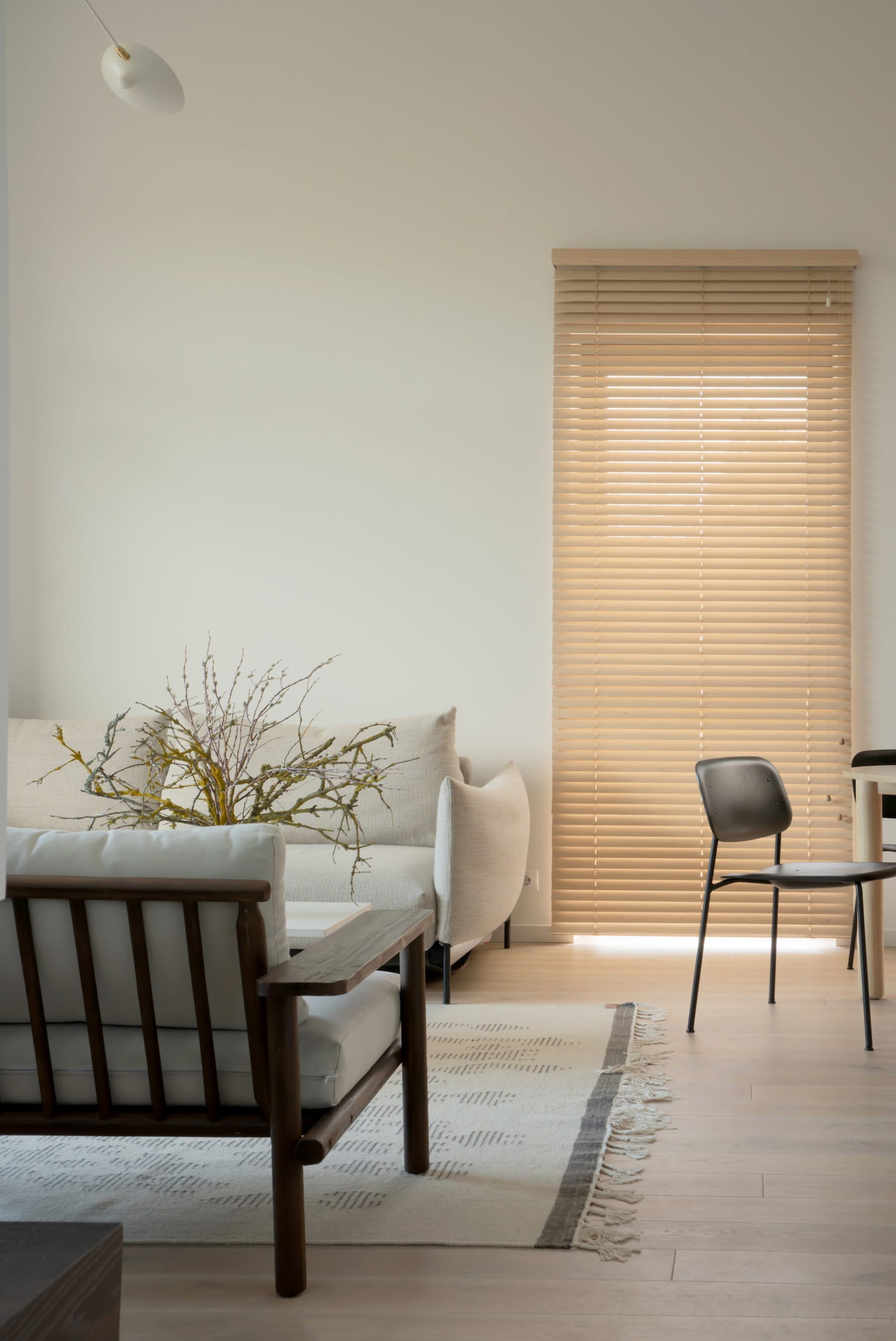Minimalist living room with wooden flooring, white walls, and a window with wooden blinds, showcasing budget-friendly design