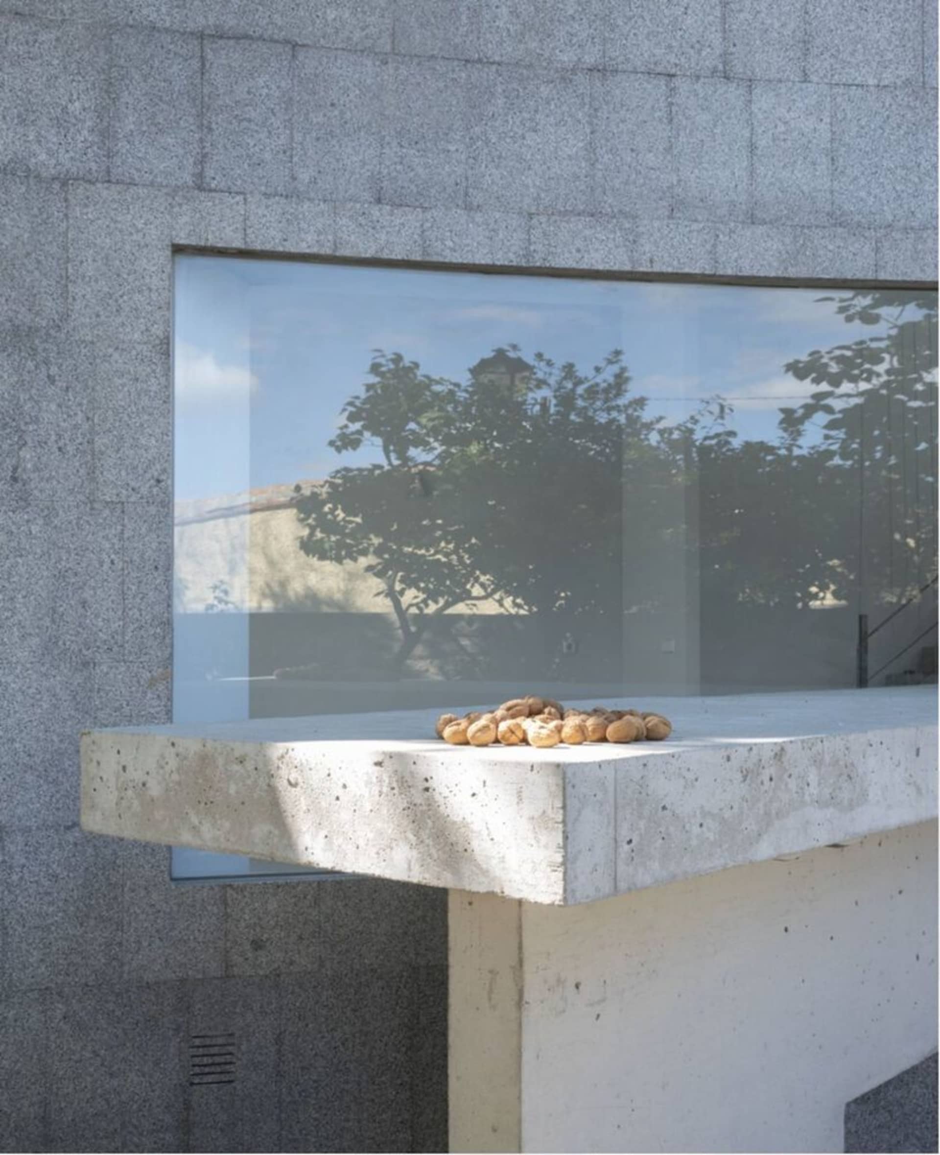 A modern exterior featuring a concrete wall with a large glass window and patio.