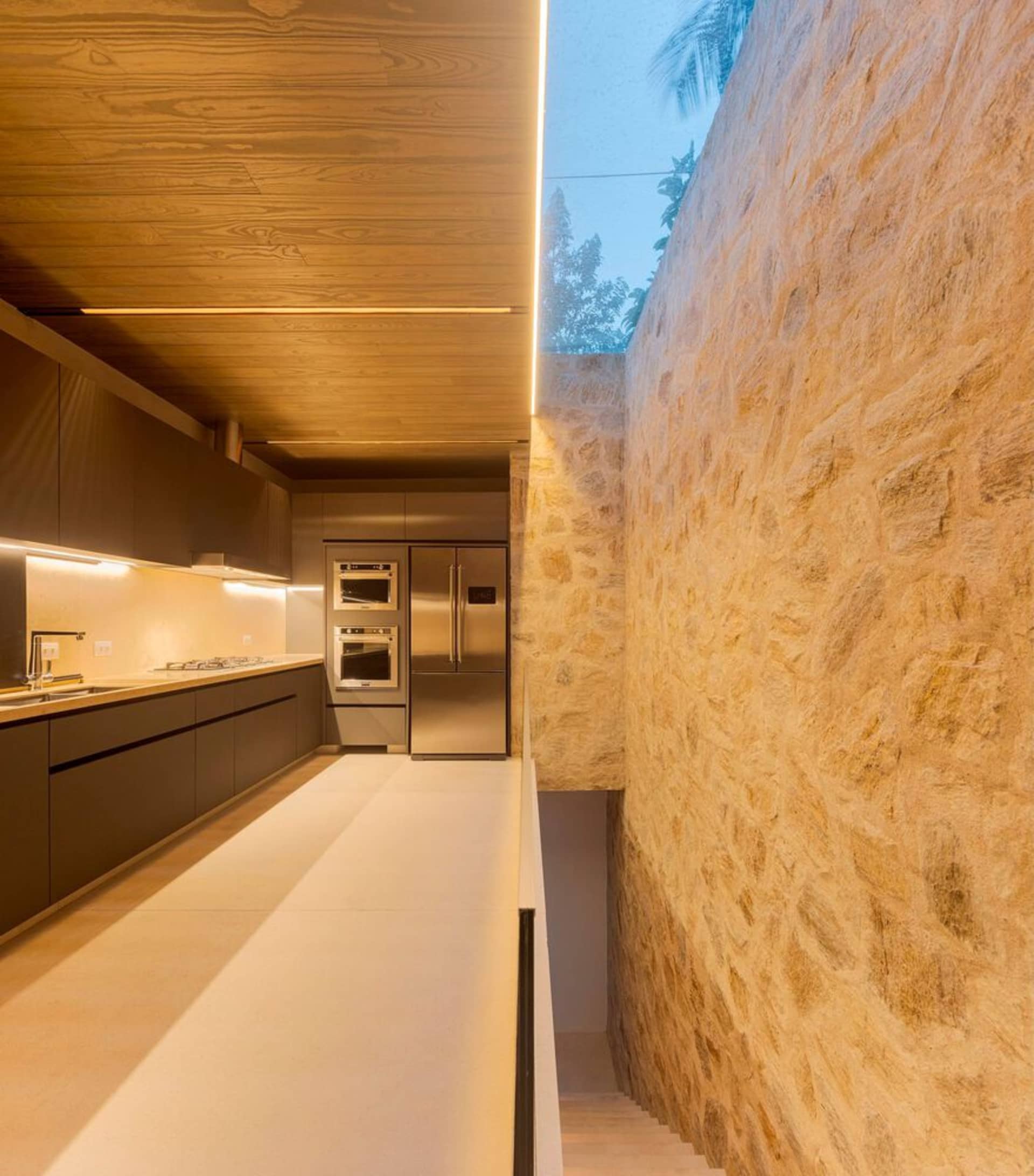A modern kitchen with stone walls, wooden ceiling, and stainless steel appliances.