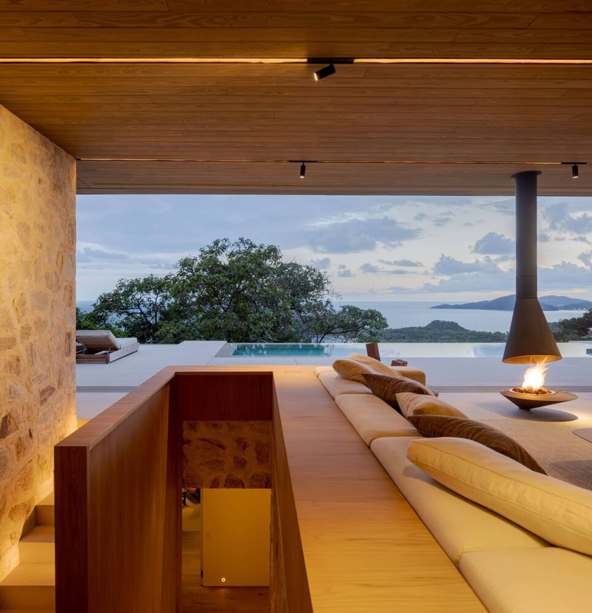 Modern living room with a sea view, featuring wood and stone materials, and a linear fireplace.