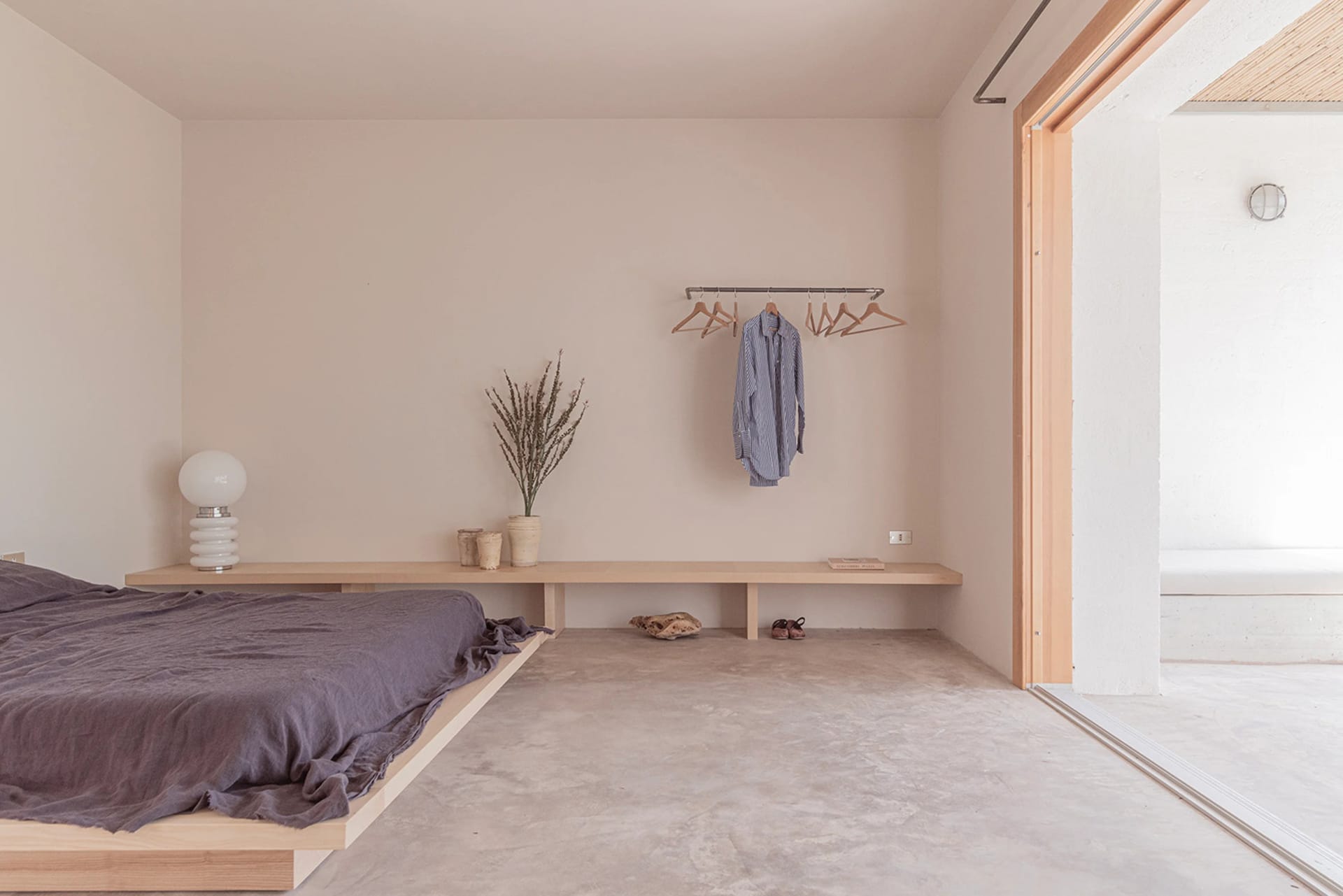 A minimalist bedroom with a concrete floor and a low wooden bed platform.