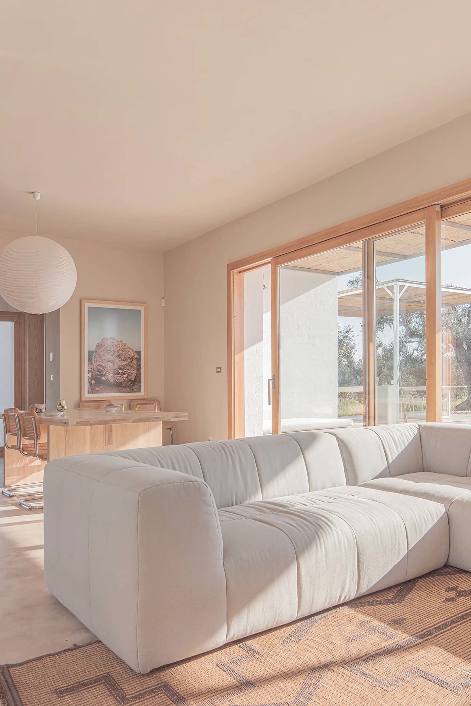 Minimalist living room with a white couch, dining table, and large windows allowing natural light to enter.