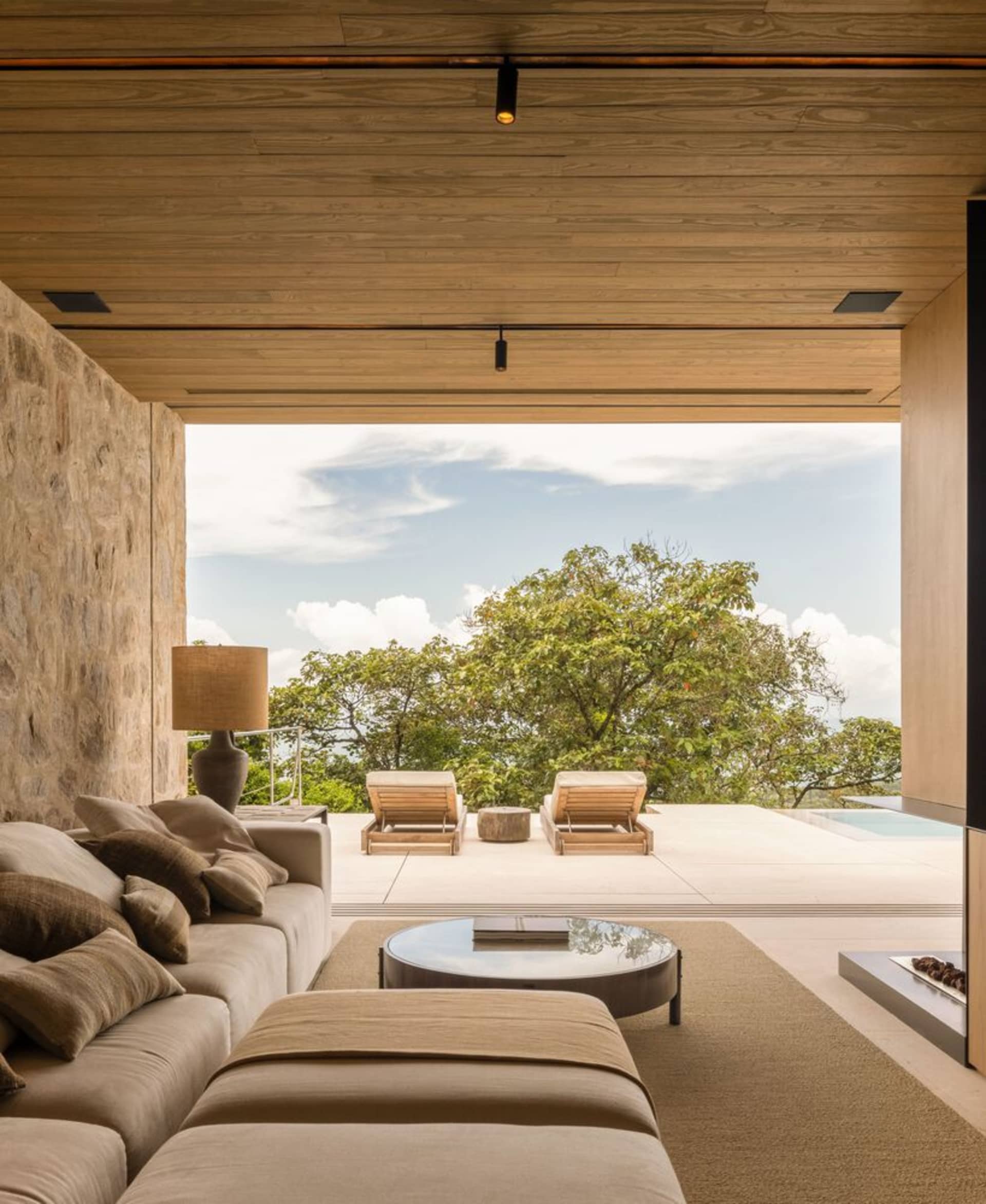 A minimalist living room featuring wood and stone materials with a comfortable seating area and a view of the outdoors.
