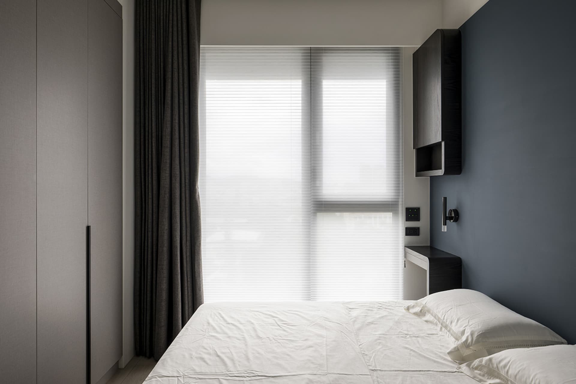 A modern bedroom with a bed, windows, and grey curtains.