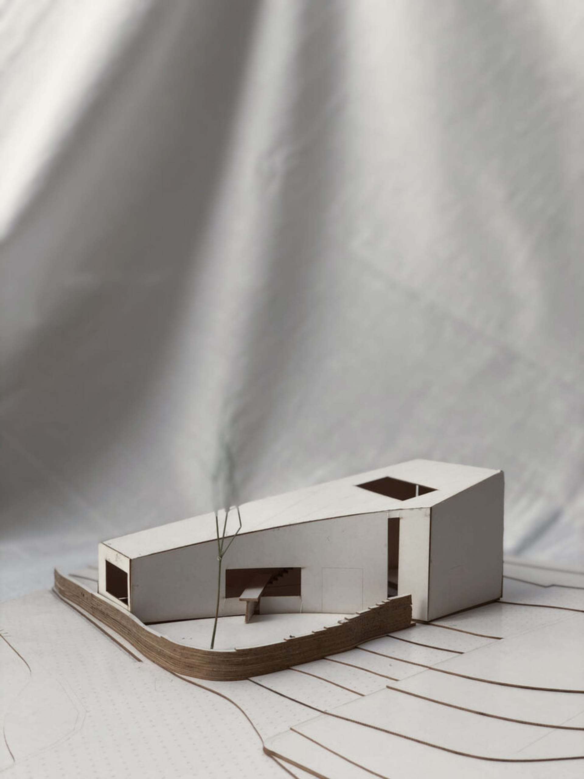 A modern residential building model crafted from cardboard materials on a white surface with floor plan layout lines.