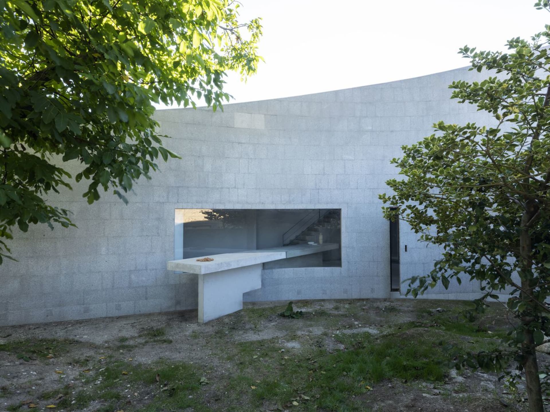 Modern residential home made of concrete with large windows and outdoor area.