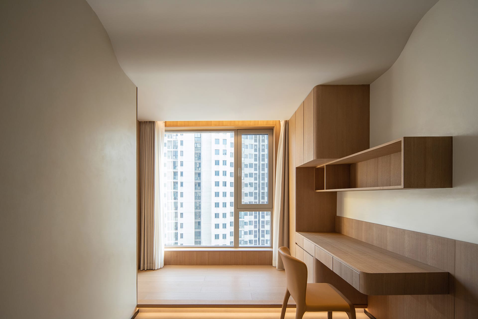 A minimalist apartment study room with a wood desk, chair, and shelving.