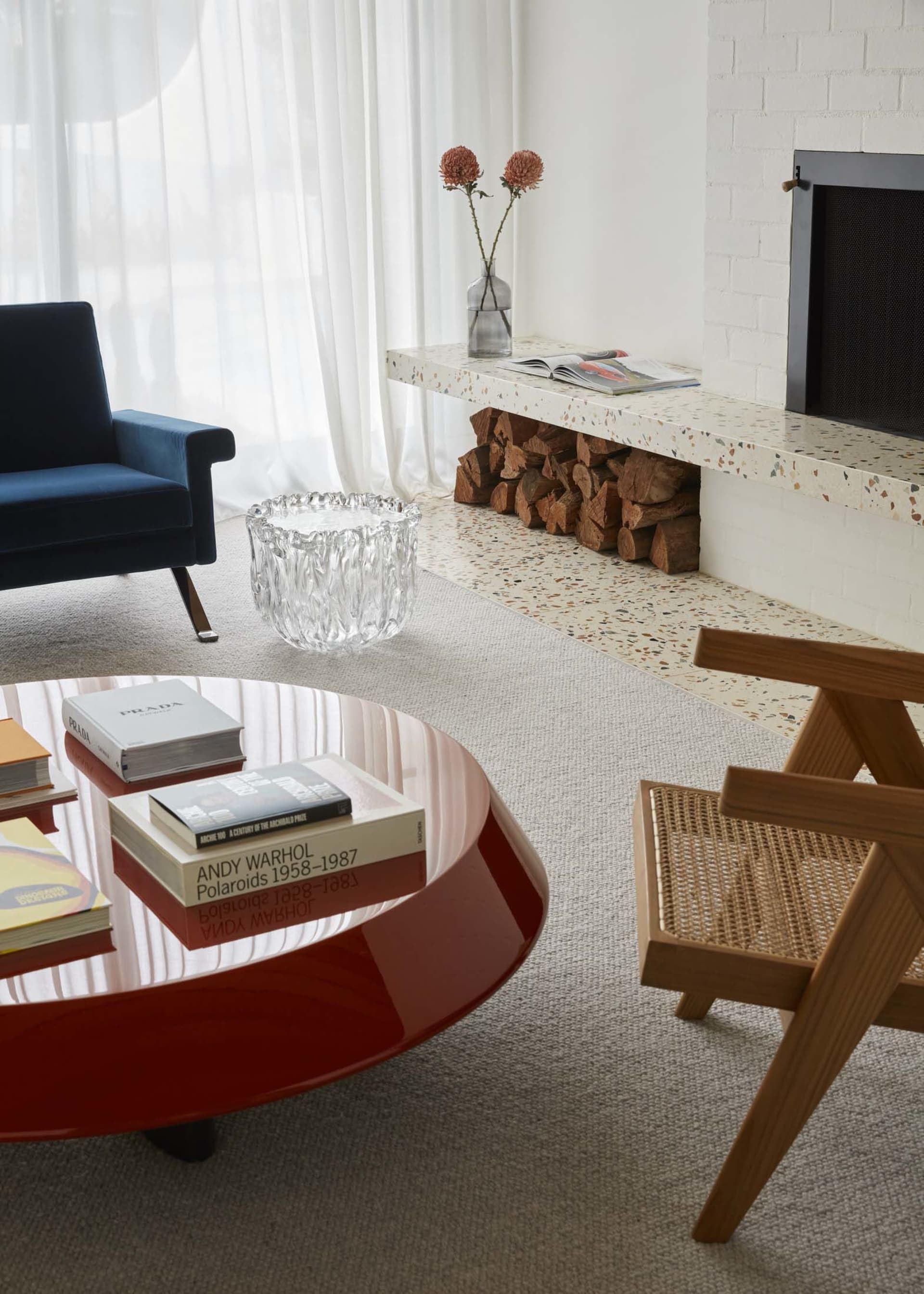 Photograph of a minimalist living room with a terrazzo floor and a sleek, rounded red coffee table.