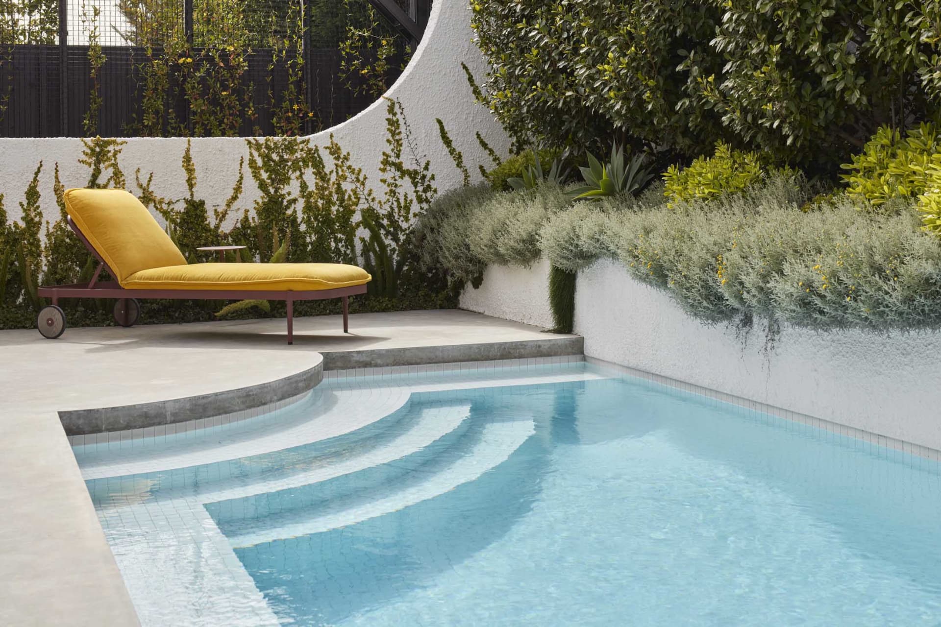 Minimalist poolside seating area with a concrete platform and yellow fabric lounge chair.