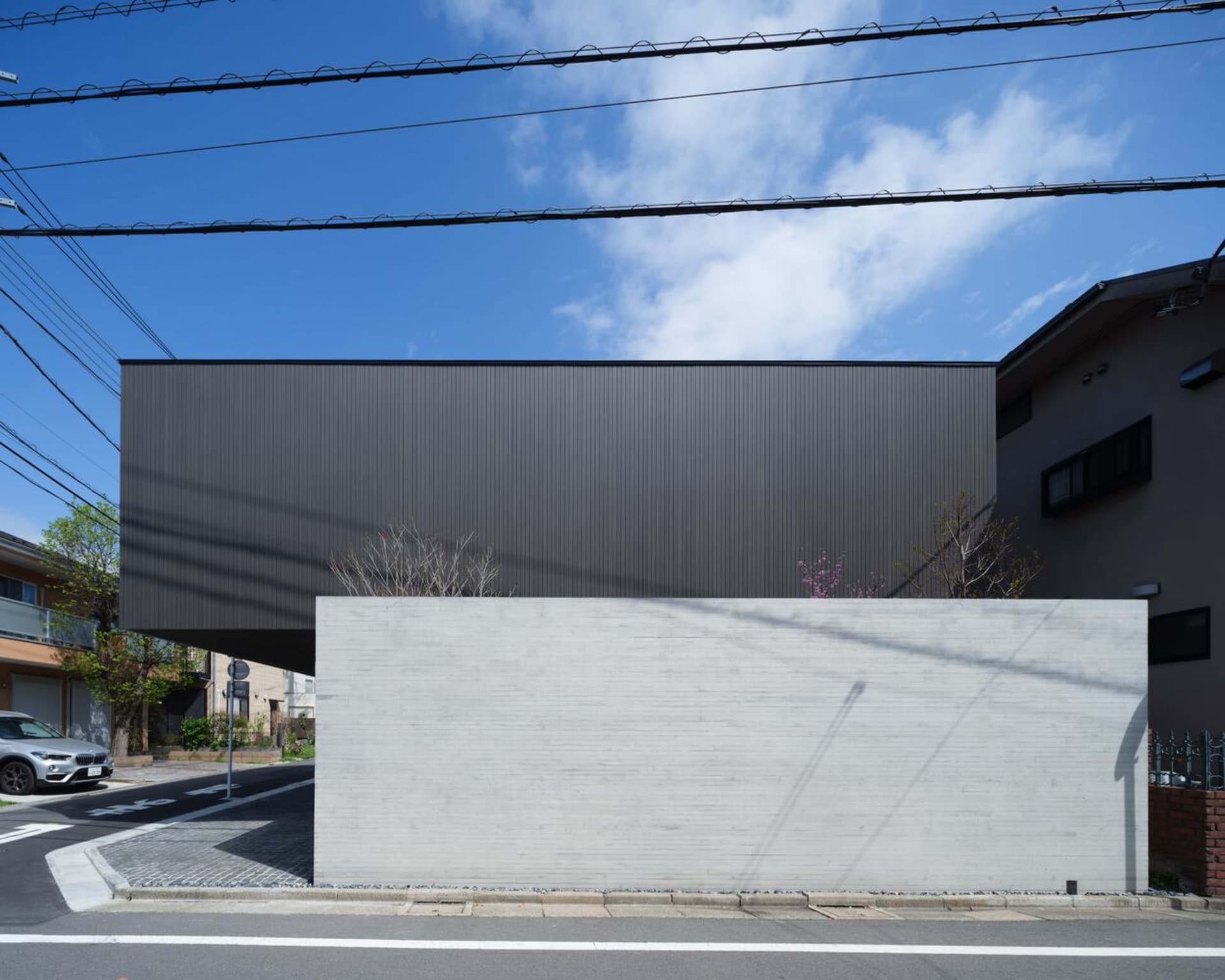 一座由混凝土打造的現代黑色盒子建築，具備極簡設計與平屋頂。