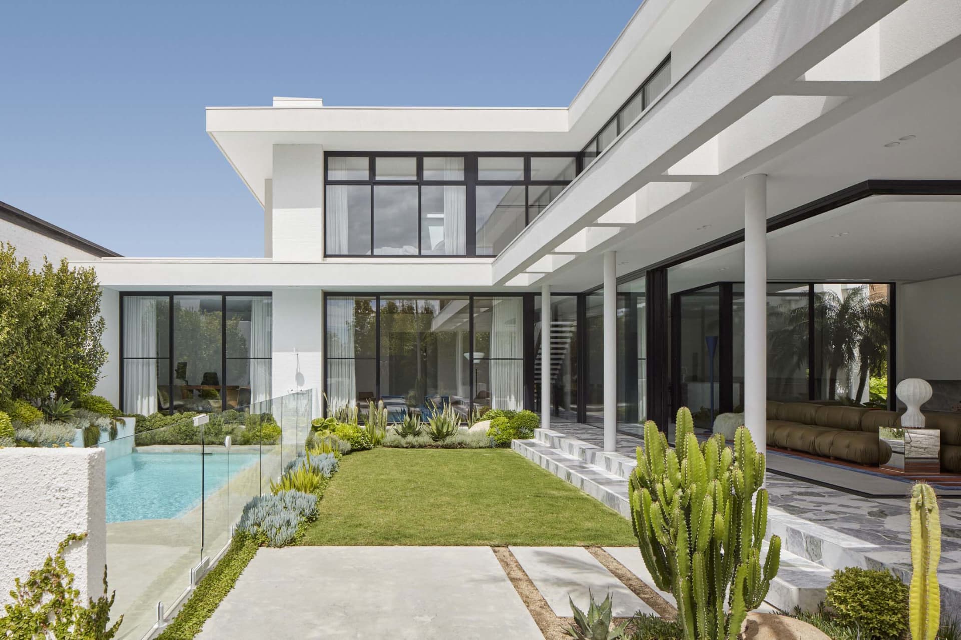 Modern residential house featuring concrete and glass materials with a large swimming pool and a well-manicured lawn.