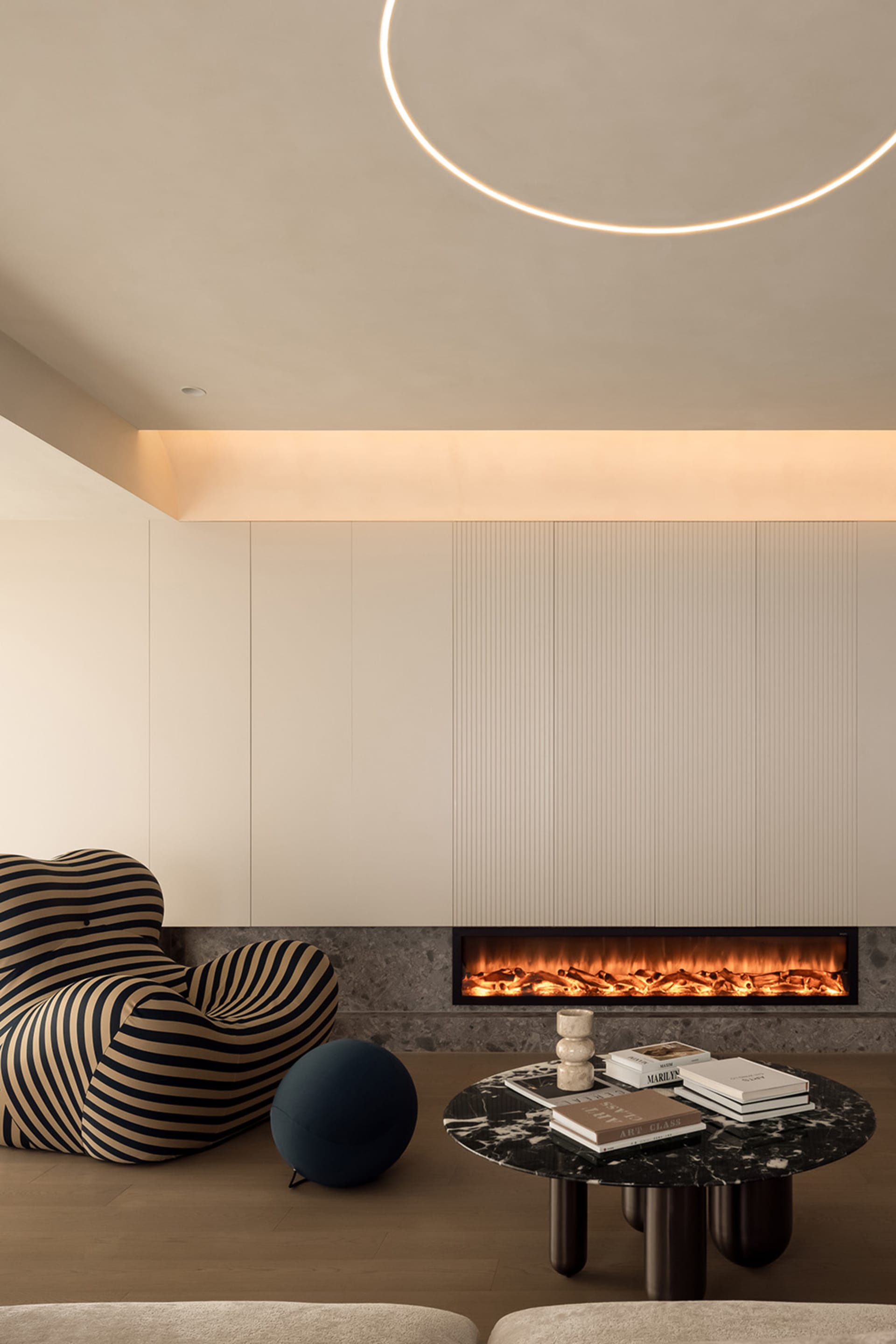 A modern minimalist living room featuring a marble fireplace and coffee table with books and decorative items.