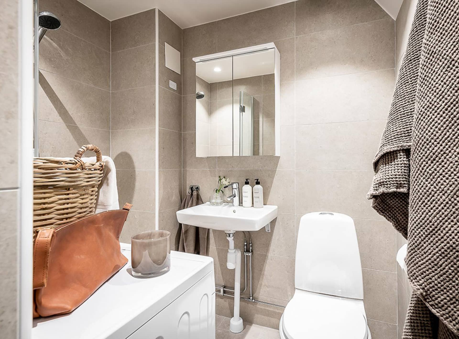 A minimalist bathroom with beige tiled walls, a white toilet, and a sink with a mirror above.